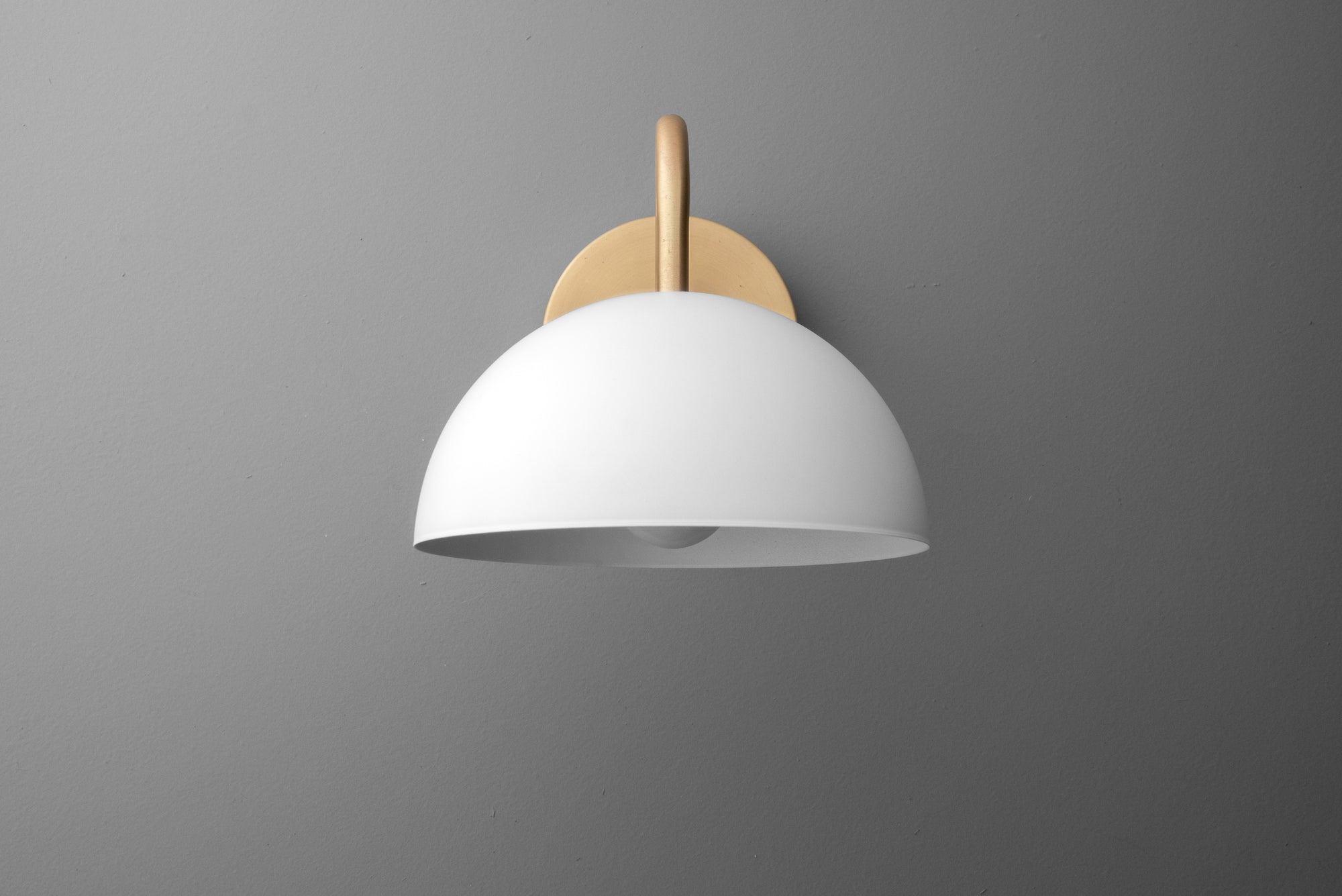 Wall sconce with a smooth, white dome shade and a warm brass mounting plate against a gray background. - SCONCE MODEL NO. 6679