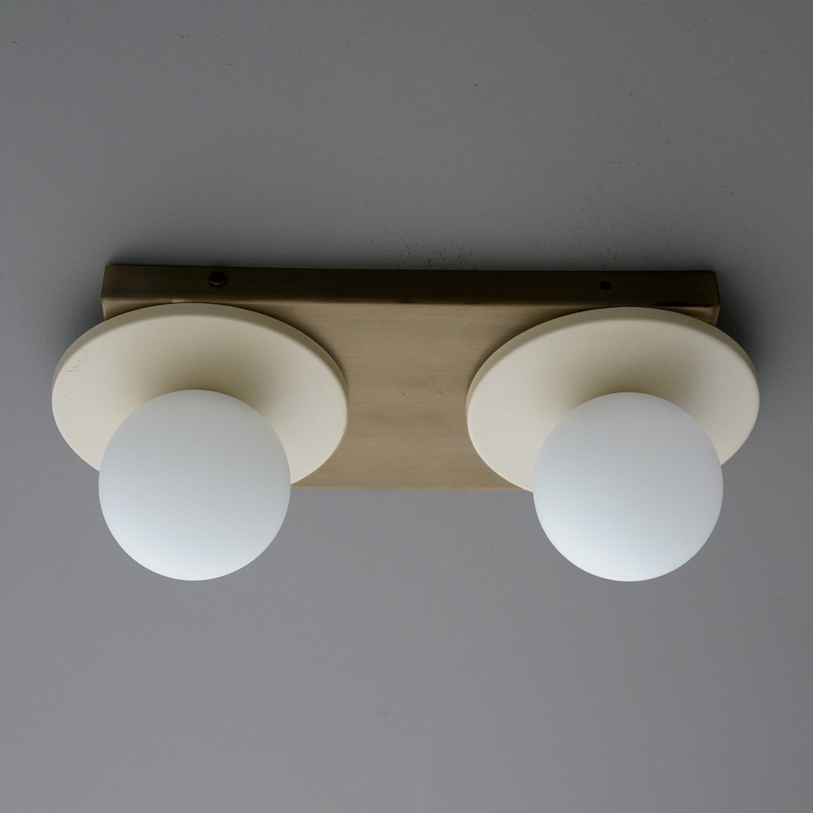 Two-light fixture mounted horizontally, with Cream round plates and opal glass globes on an Antique Brass backplate. - SCONCE MODEL NO. 8828