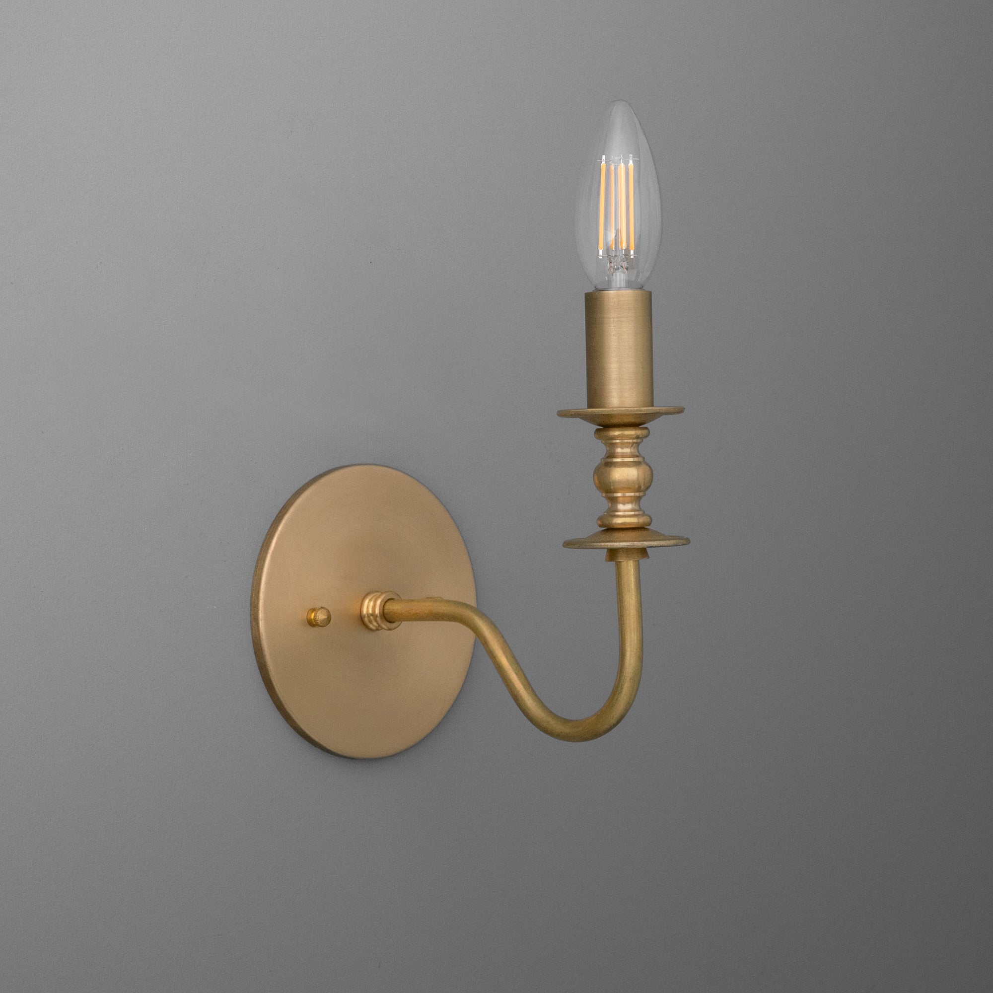 Brushed gold metal wall sconce with curved arm and single exposed candle-style bulb. - SCONCE MODEL NO. 9915