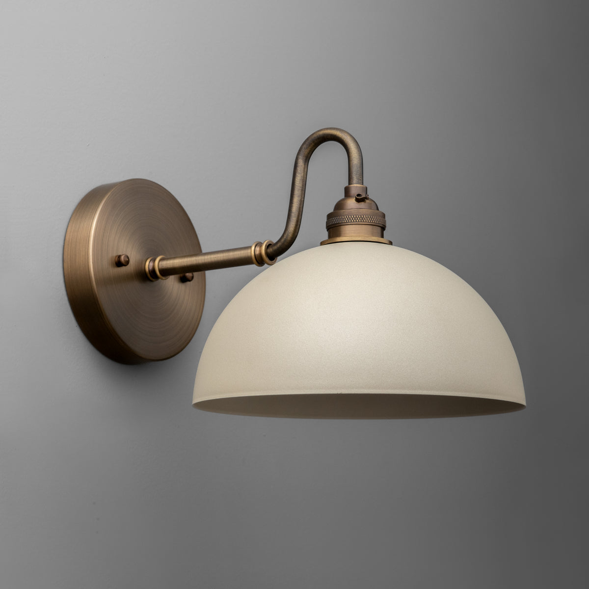 Wall sconce with antique brass finish and cream dome-shaped glass shade mounted on curved arm. - SCONCE MODEL NO. 9103