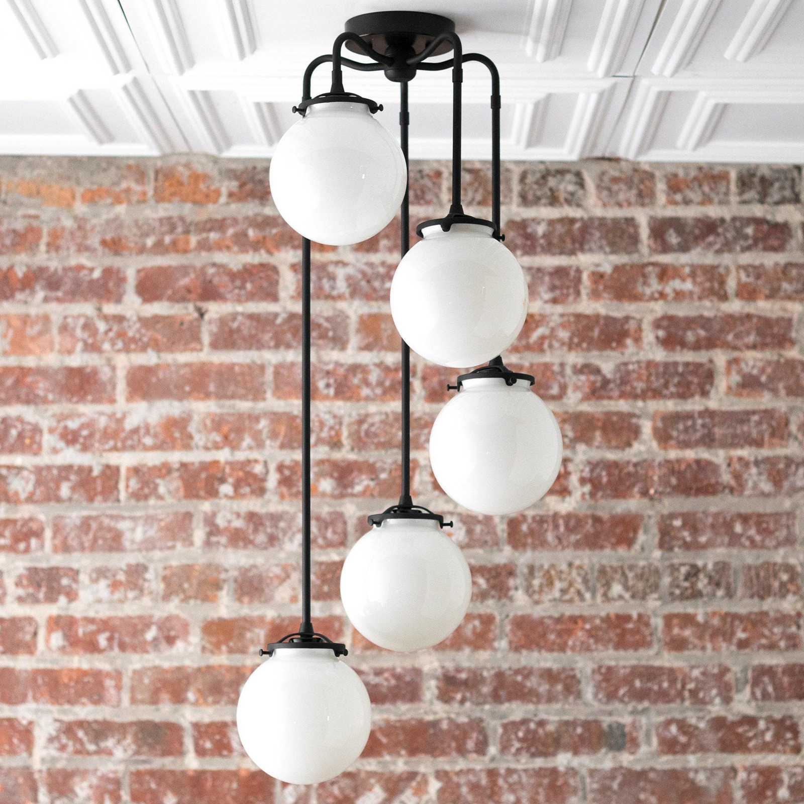 Mid-century modern chandelier with four white globe lights suspended by black metal rods against a brick wall. - CHANDELIER MODEL NO. 1809