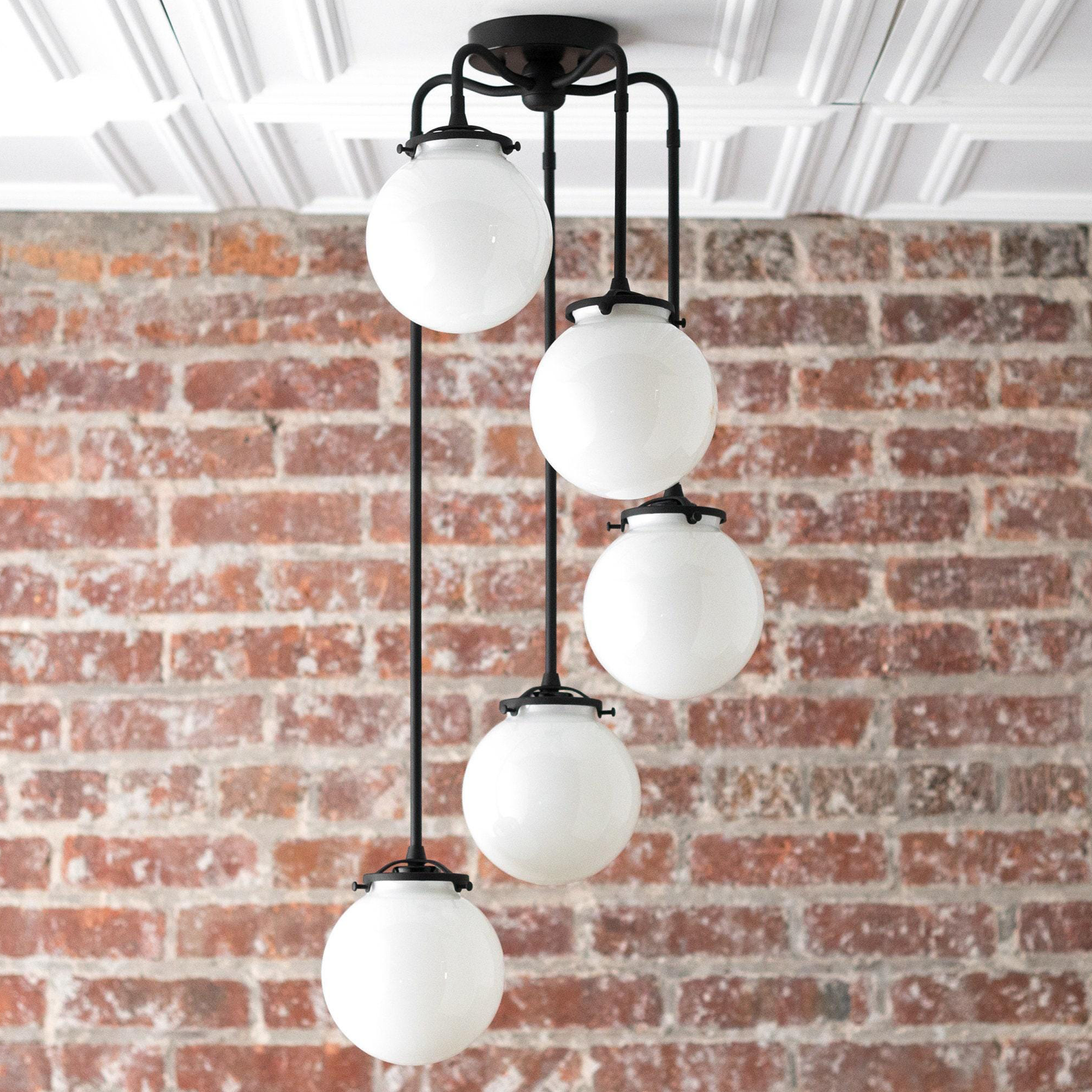 Mid-century modern chandelier with four white globe lights suspended by black metal rods against a brick wall. - CHANDELIER MODEL NO. 1809