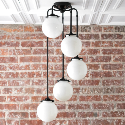 Mid-century modern chandelier with four white globe lights suspended by black metal rods against a brick wall. - CHANDELIER MODEL NO. 1809