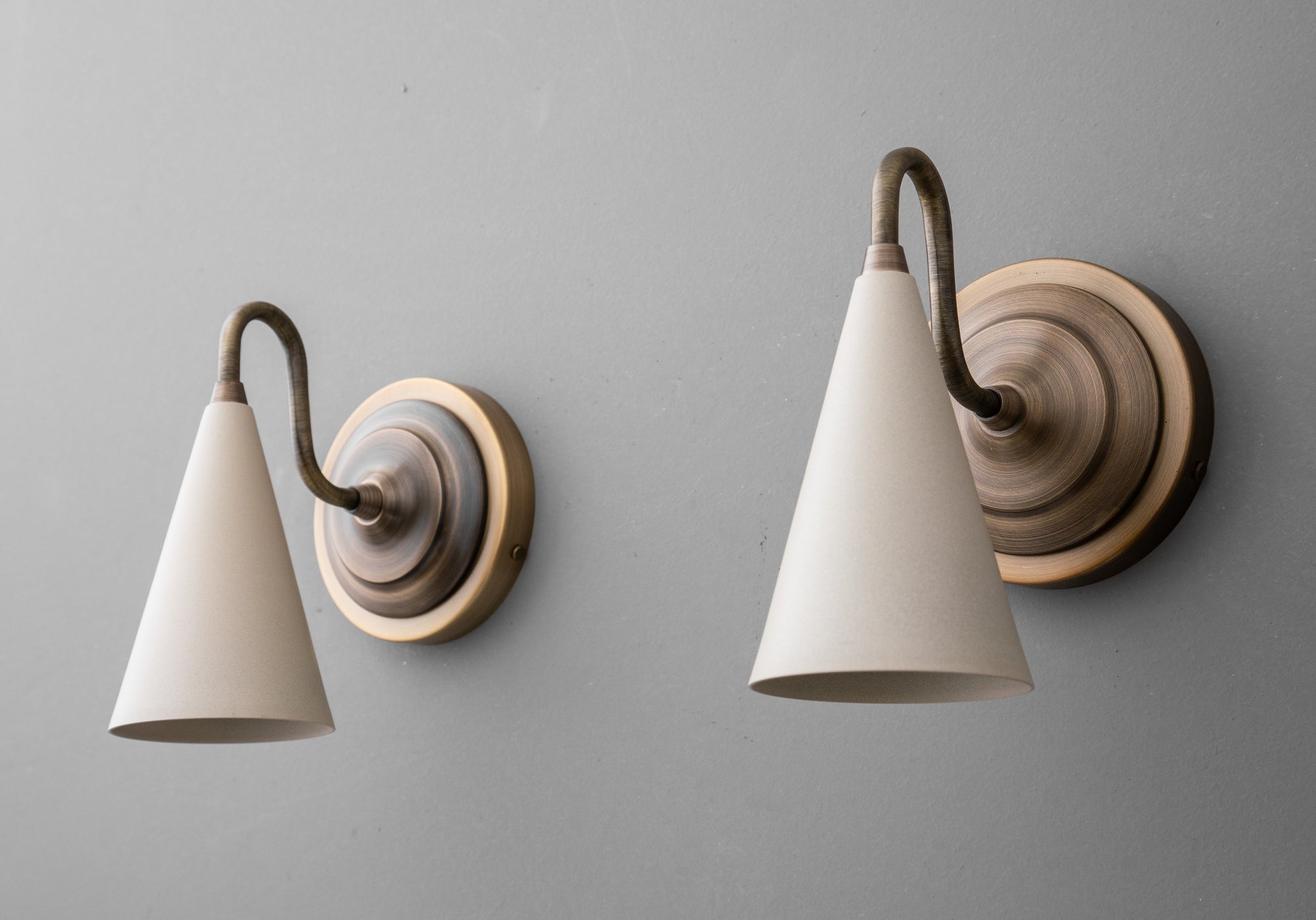 Antique brass sconce with cream cone-shaped shade and curved arm on round backplate. - Sconce Model No. 6790