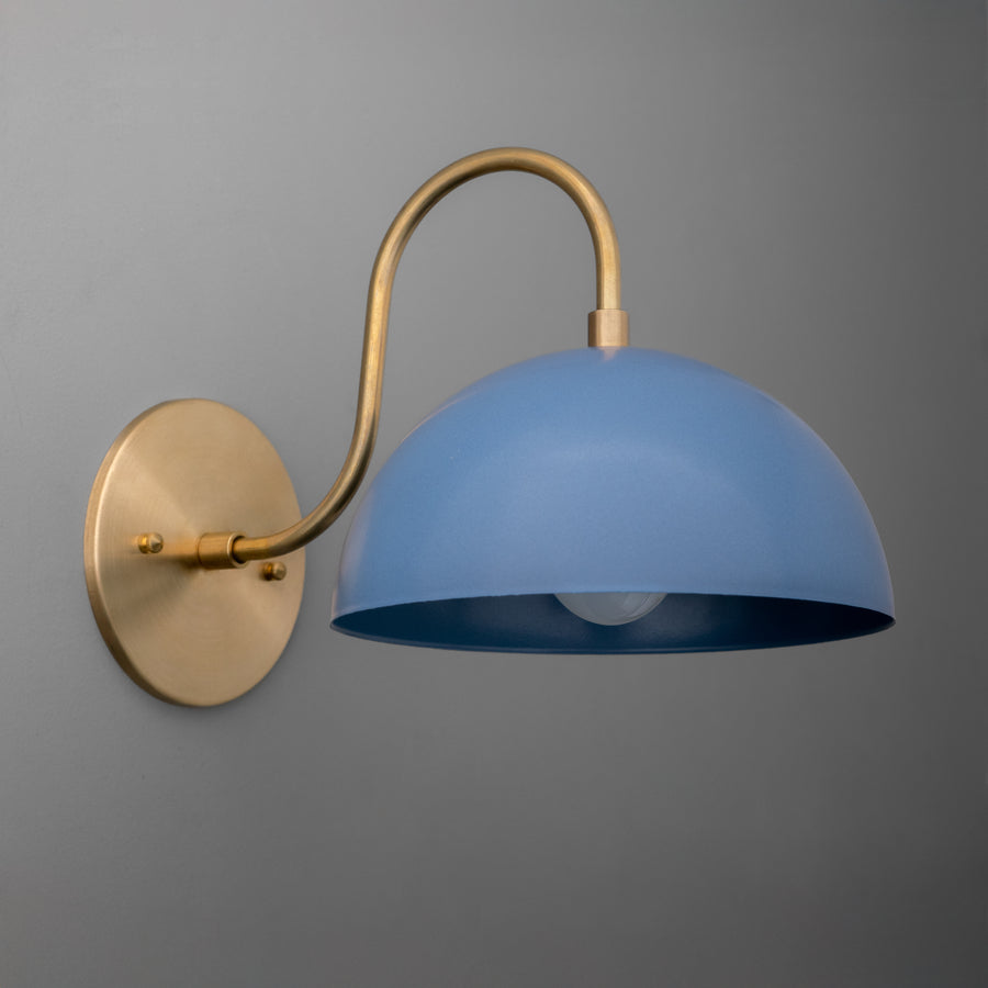 Raw brass wall sconce with a curved arm and a dome-shaped periwinkle blue shade against a gray background. - SCONCE MODEL NO. 9092