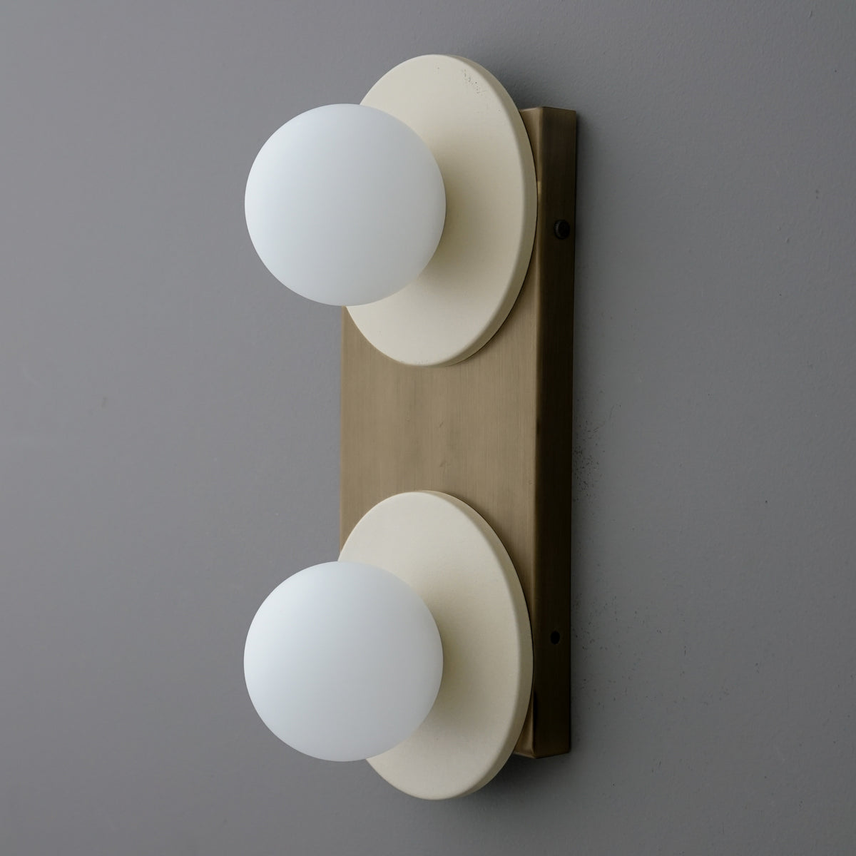 Angled side view of a two-light sconce with Cream round plates and opal glass globes on an Antique Brass backplate. - SCONCE MODEL NO. 8828