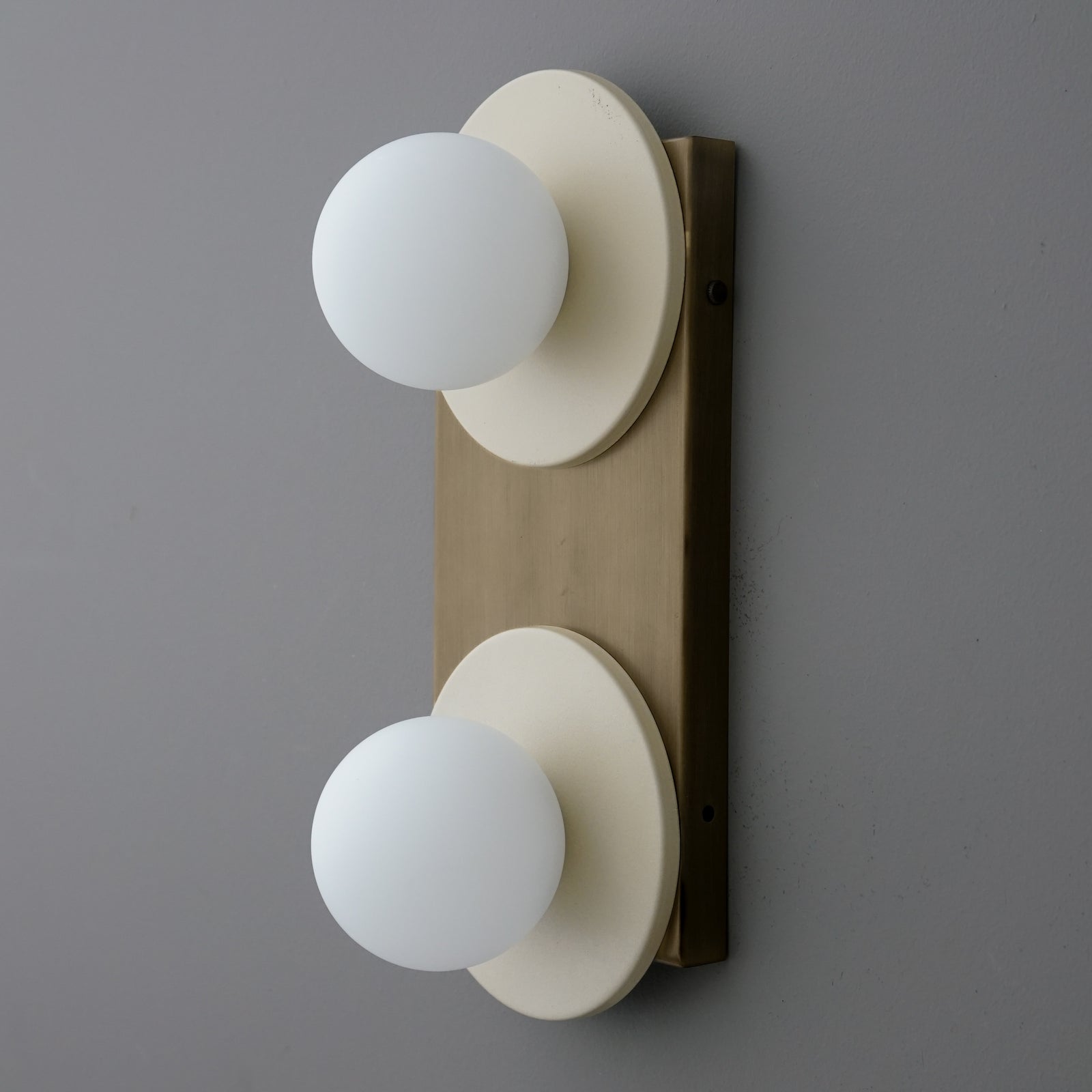Angled side view of a two-light sconce with Cream round plates and opal glass globes on an Antique Brass backplate. - SCONCE MODEL NO. 8828