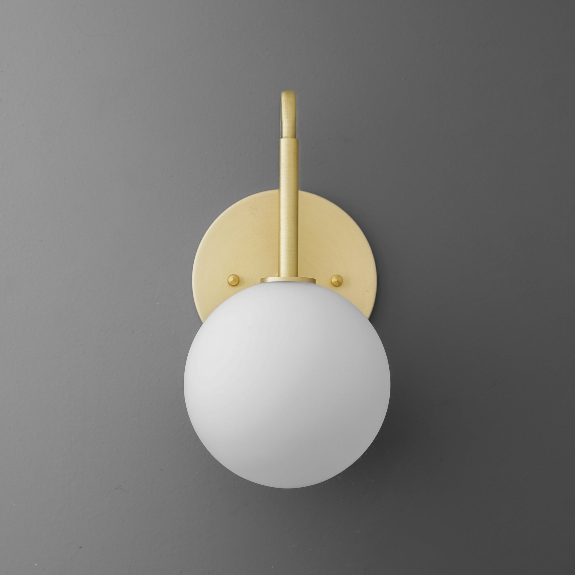 Wall sconce with matte white glass globe and polished brass fixture on gray wall. - SCONCE MODEL NO. 9105