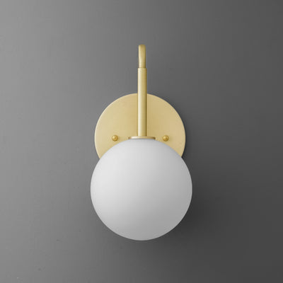 Wall sconce with matte white glass globe and polished brass fixture on gray wall. - SCONCE MODEL NO. 9105