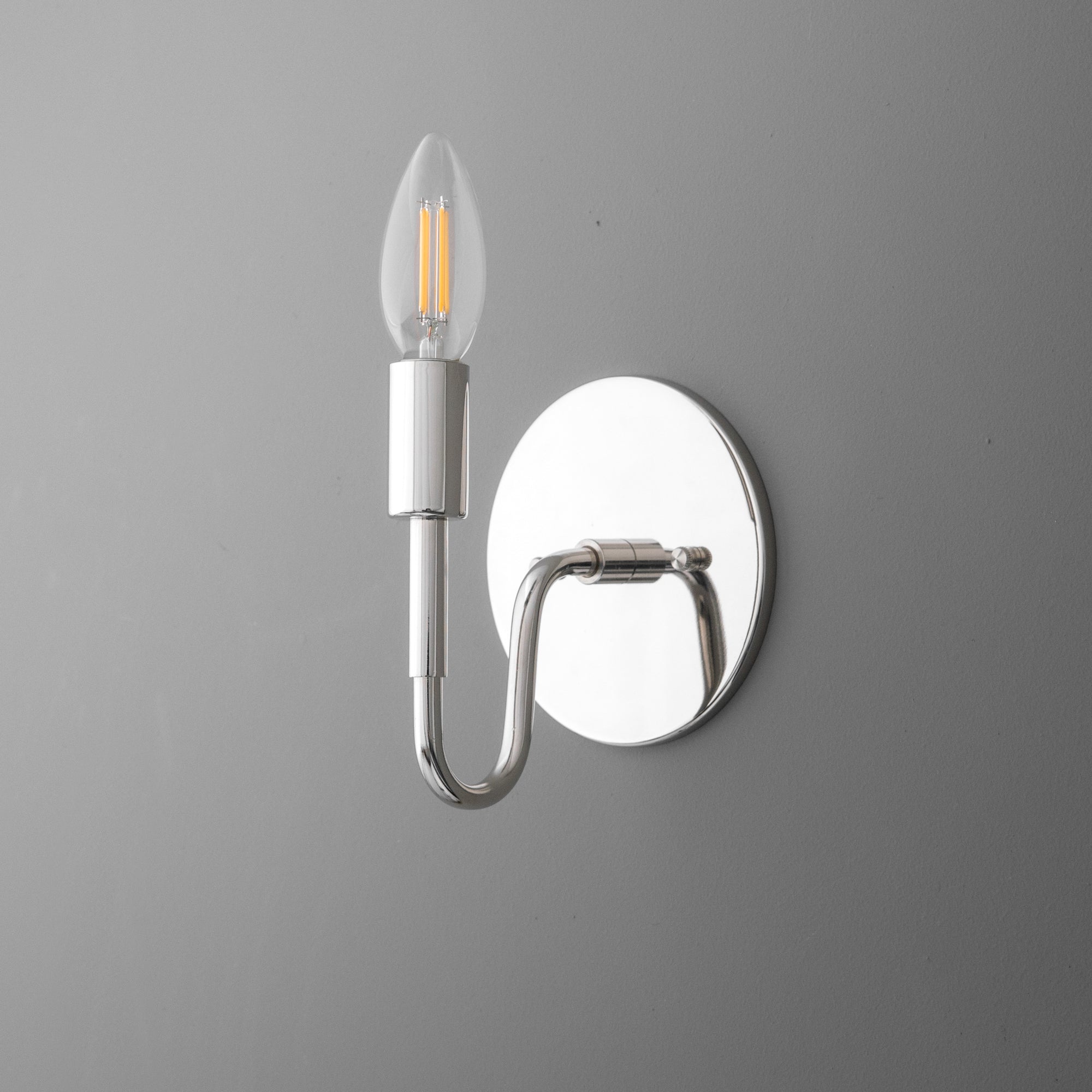 Polished chrome wall sconce with a curved arm and exposed candle-style LED bulb. - SCONCE MODEL NO. 1100