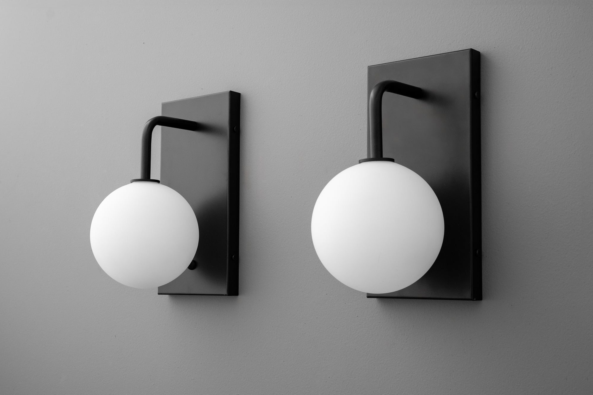 Black metal wall sconces with matte white spherical glass shades mounted on rectangular backplates. - SCONCE MODEL NO. 9002