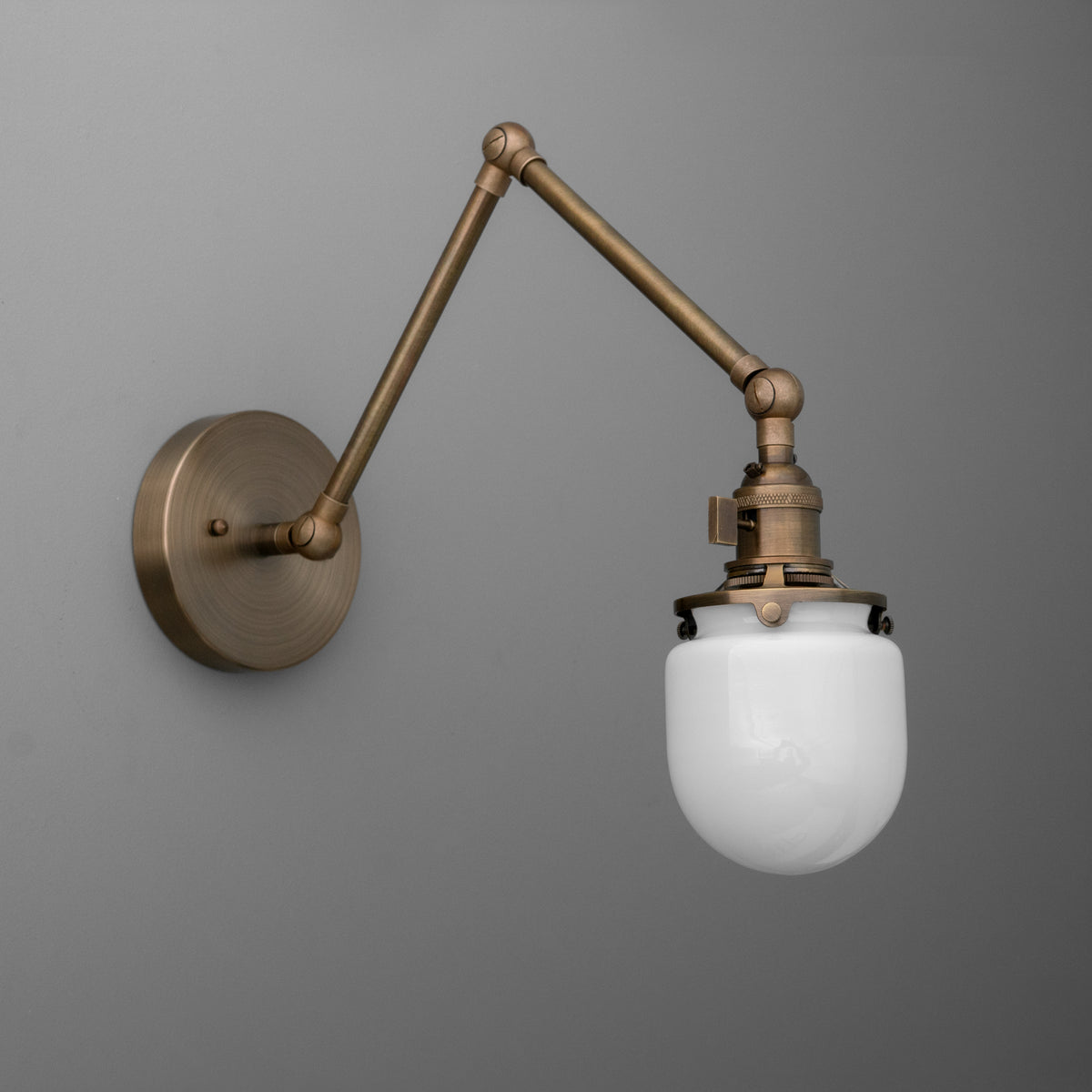 Adjustable antique brass wall sconce with white opal glass globe shade and industrial-style arm. - SCONCE MODEL NO. 7575