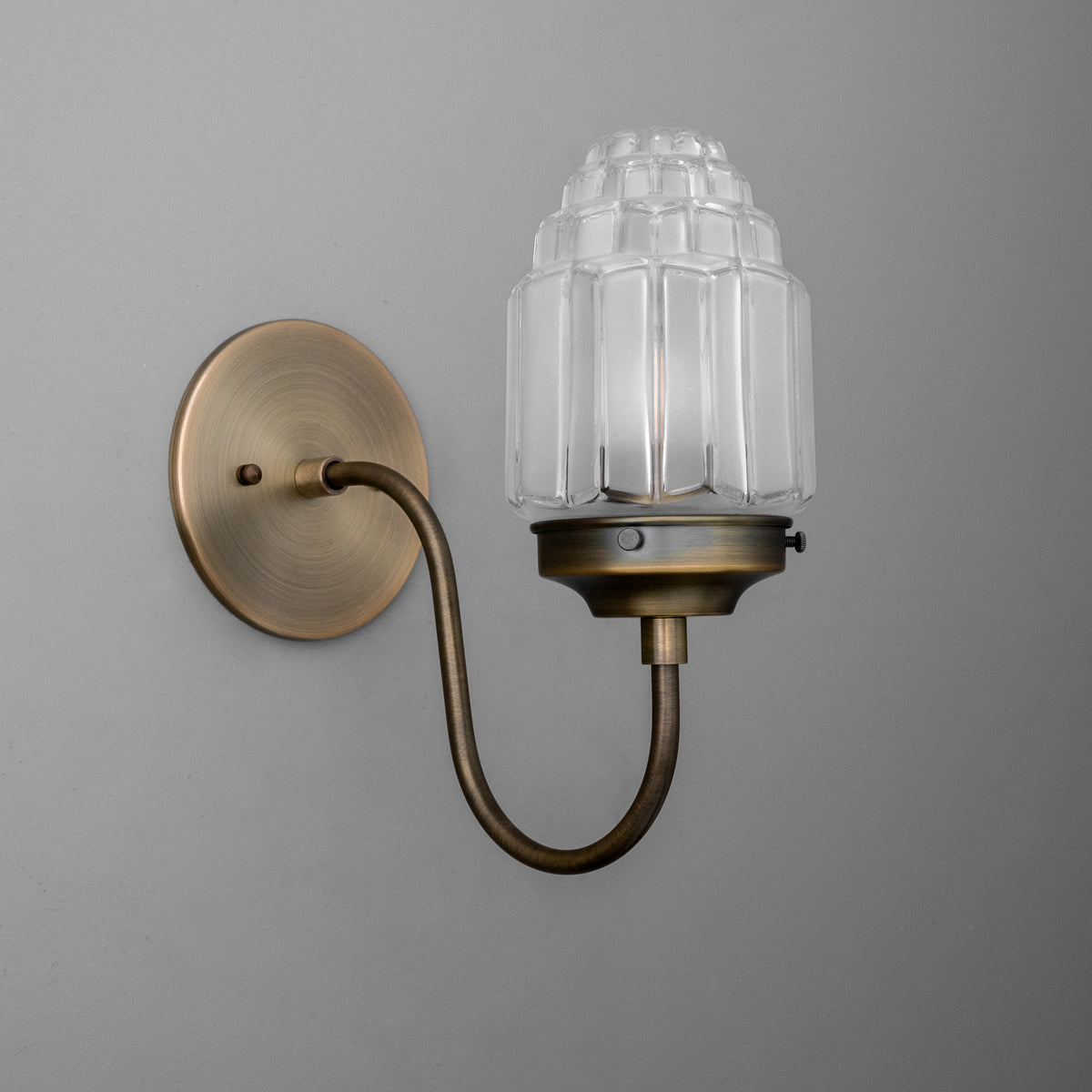 Antique brass wall sconce with curved arm and ribbed clear glass shade, single bulb design. - SCONCE MODEL NO. 1074