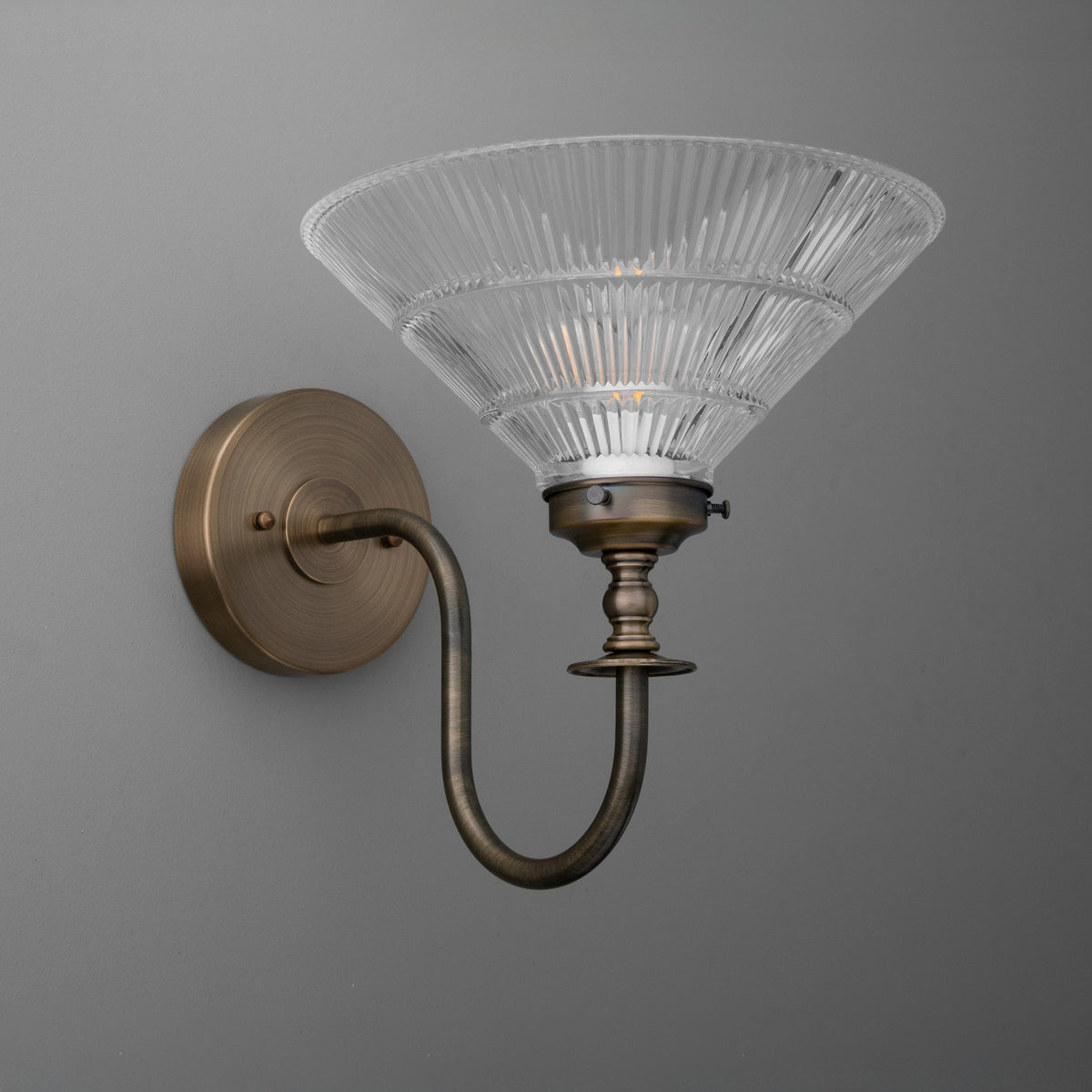 Antique brass sconce with curved arm and ribbed clear glass shade in flared cone shape. - SCONCE MODEL NO. 8036