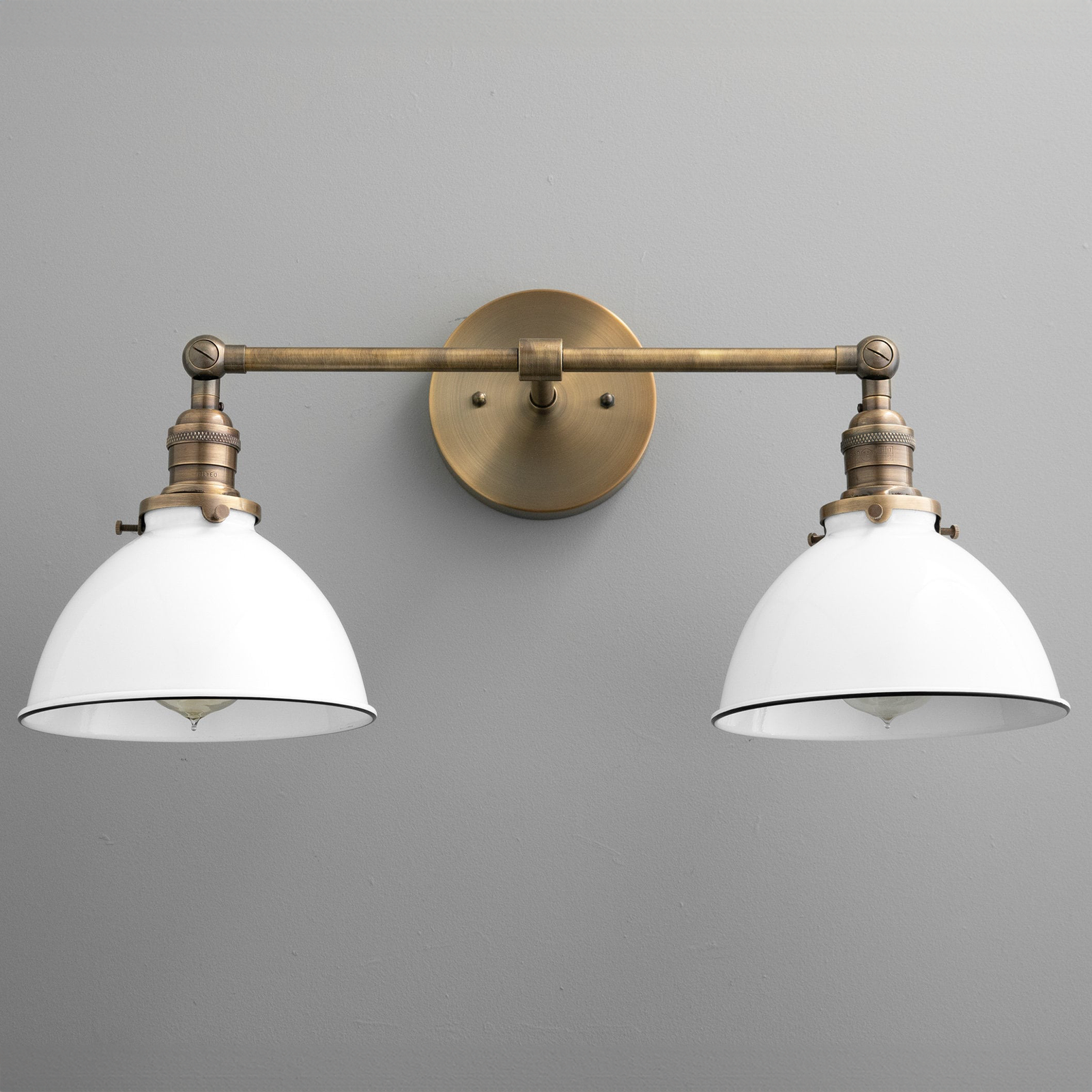 Two-bulb vanity light with antique brass finish and white industrial-style metal shades mounted on gray wall. - VANITY LIGHT MODEL NO. 4564