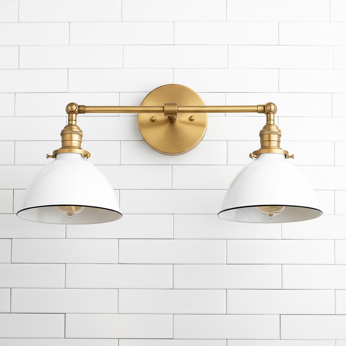 Two-light vanity fixture with antique brass finish and white metal shades against white subway tile wall. - VANITY LIGHT MODEL NO. 4564