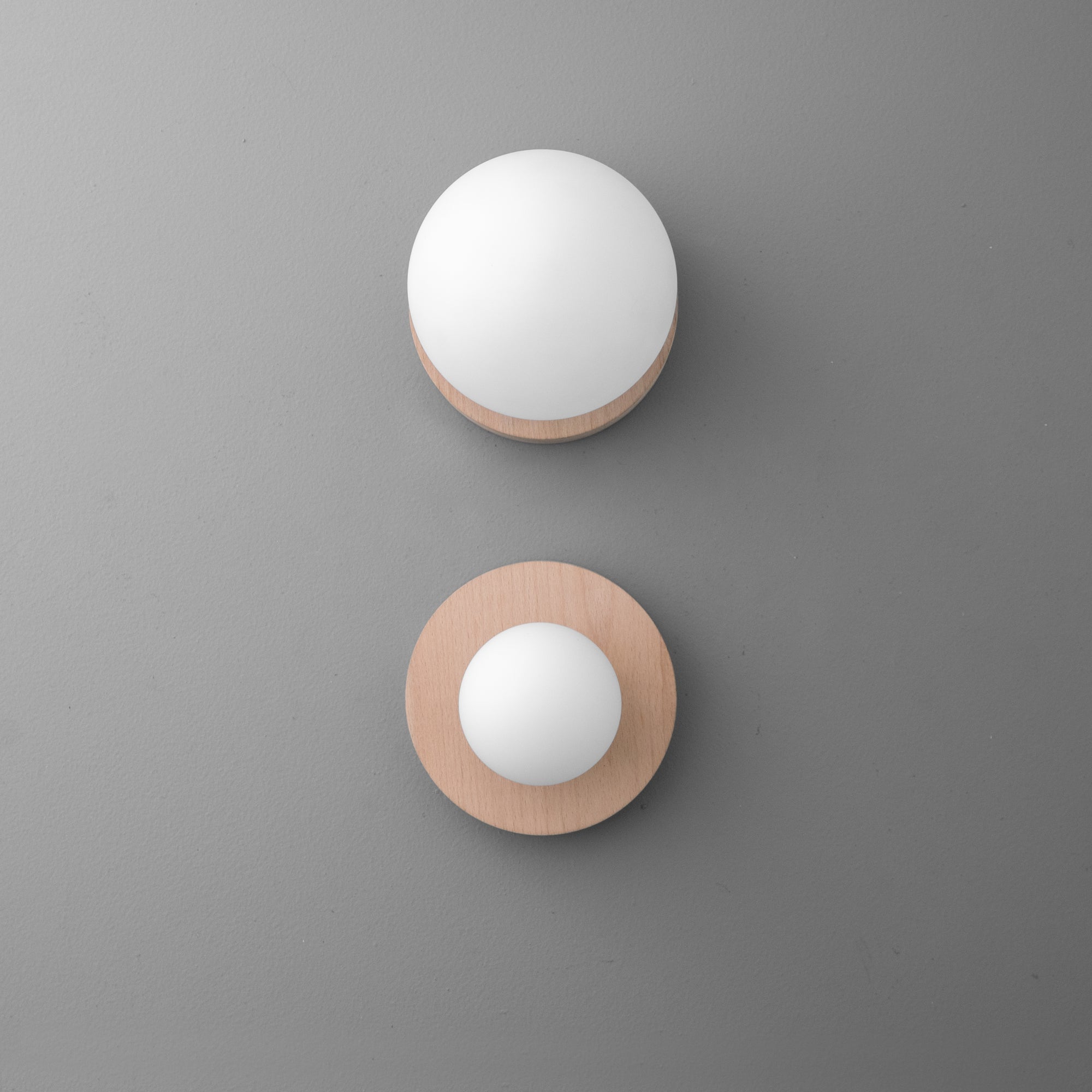 Minimalist wall sconces with round white glass globes and natural wood bases against gray wall. - SCONCE MODEL NO. 4943