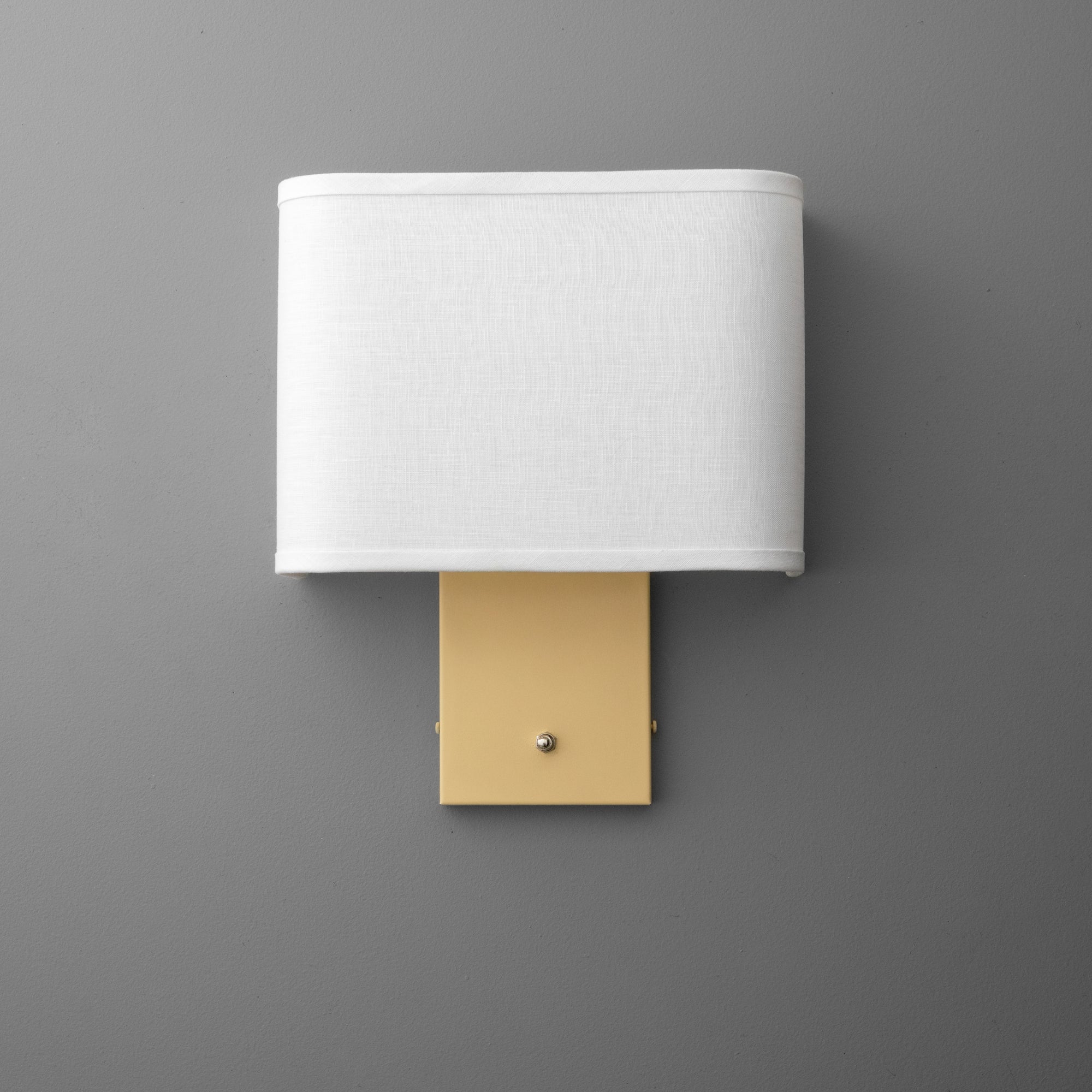 Wall sconce with white fabric rectangular shade and matte yellow brass rotary base on gray background. - SCONCE MODEL NO. 7769