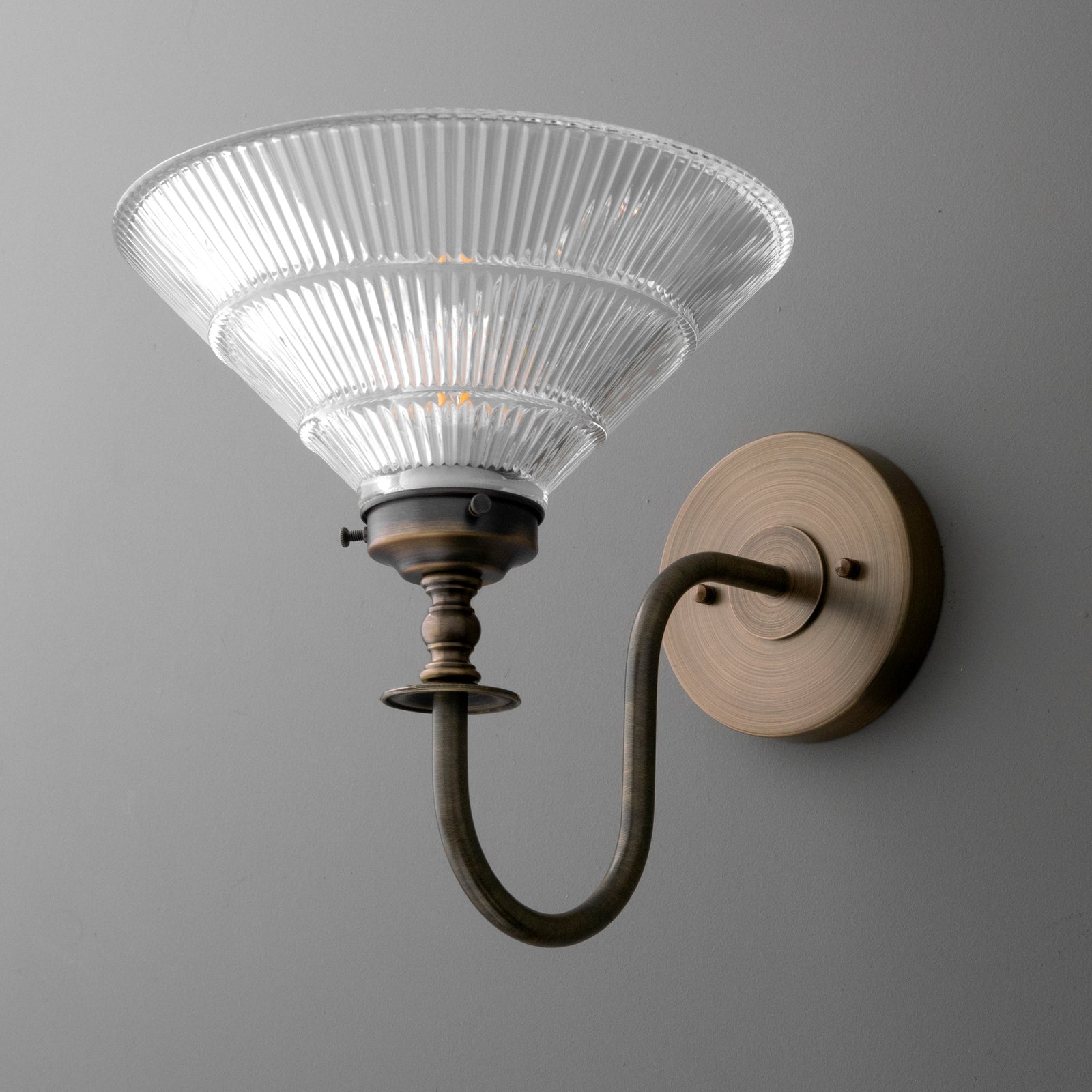 Antique brass wall sconce with curved arm and ribbed clear glass shade. - SCONCE MODEL NO. 8036