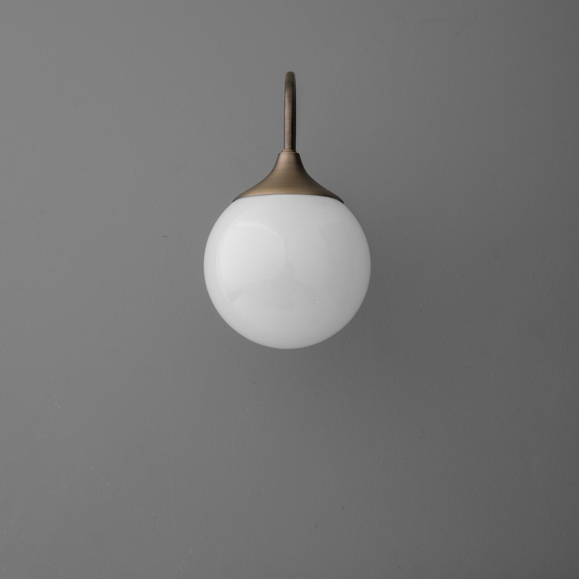 Wall-mounted sconce with round white glass globe and antique brass arm against gray background. - SCONCE MODEL NO. 3961
