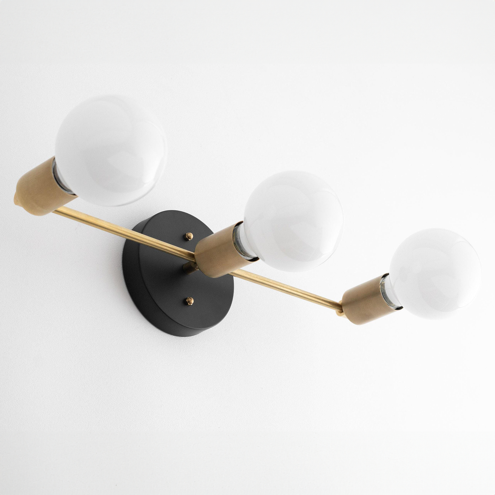 Mid-century modern 3-bulb vanity light with black circular base and raw brass arms. - VANITY LIGHT MODEL NO. 0518