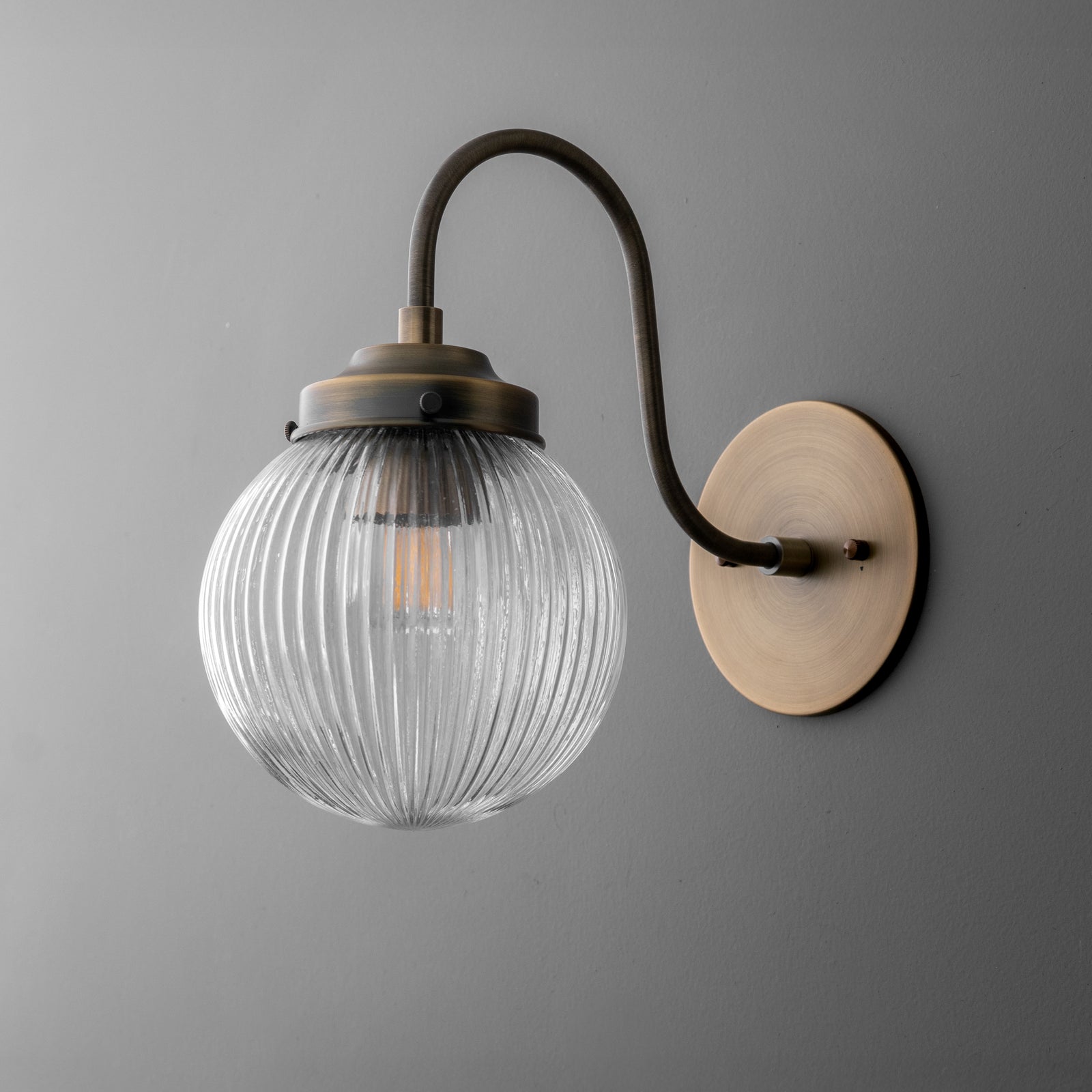Wall sconce with ribbed clear glass globe and curved antique brass arm on round backplate. - SCONCE MODEL NO. 0691