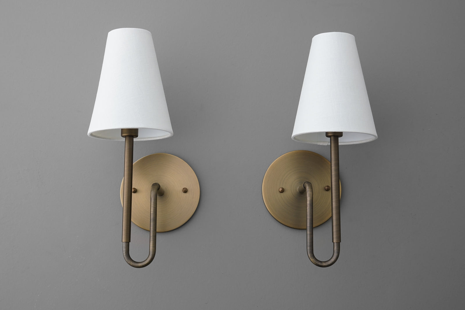 Pair of brass wall sconces with white tapered fabric shades and round backplates, modern design. - SCONCE MODEL NO. 1008