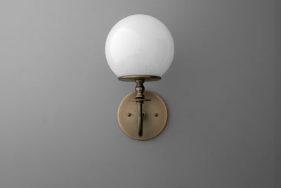 Wall sconce with antique brass finish and round white glass globe shade. - SCONCE MODEL NO. 7857