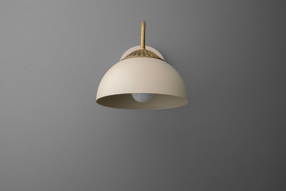 Raw brass wall sconce with cream dome-shaped shade and minimalist curved arm on gray background. - SCONCE MODEL NO. 9408