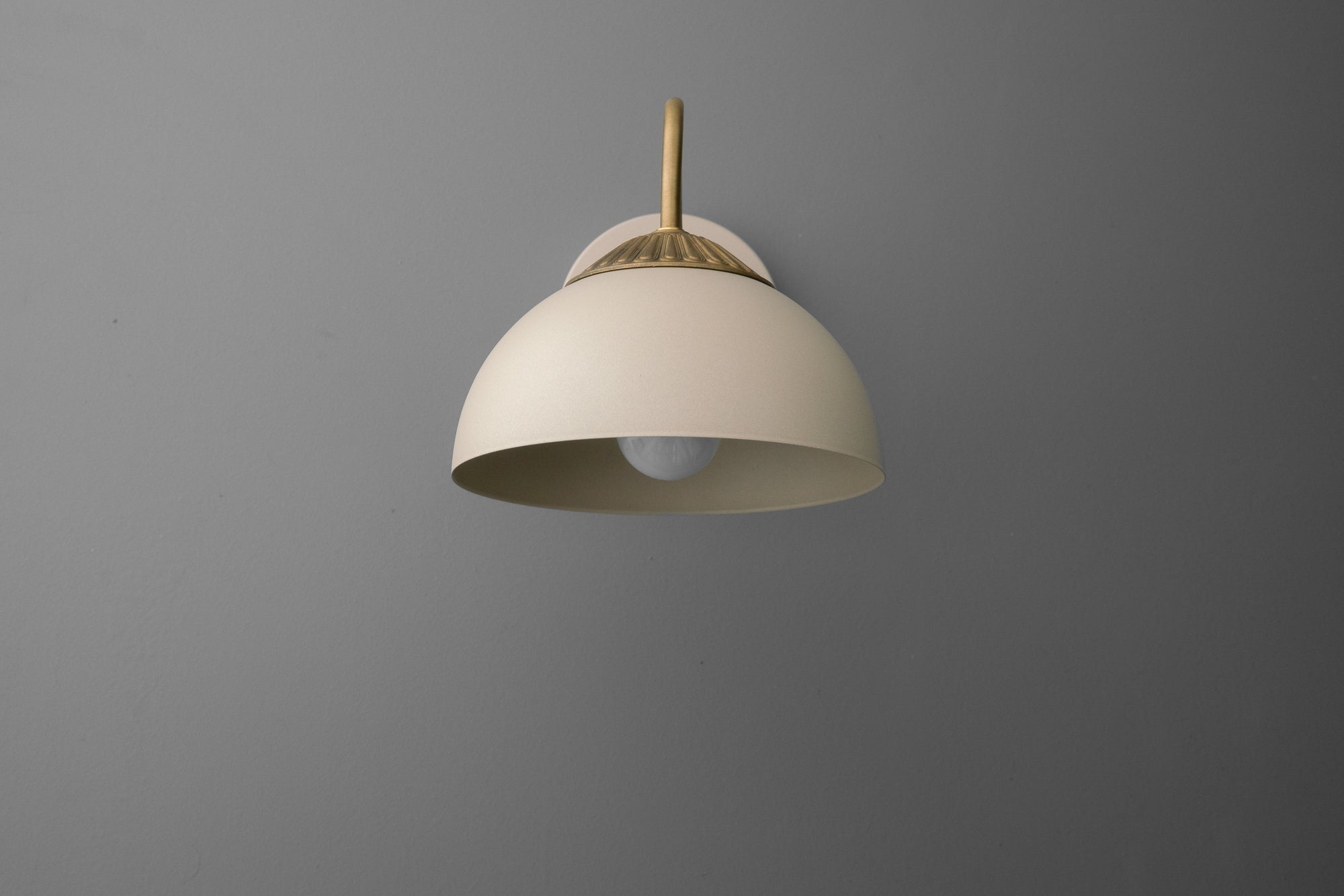 Raw brass wall sconce with cream dome-shaped shade and minimalist curved arm on gray background. - SCONCE MODEL NO. 9408