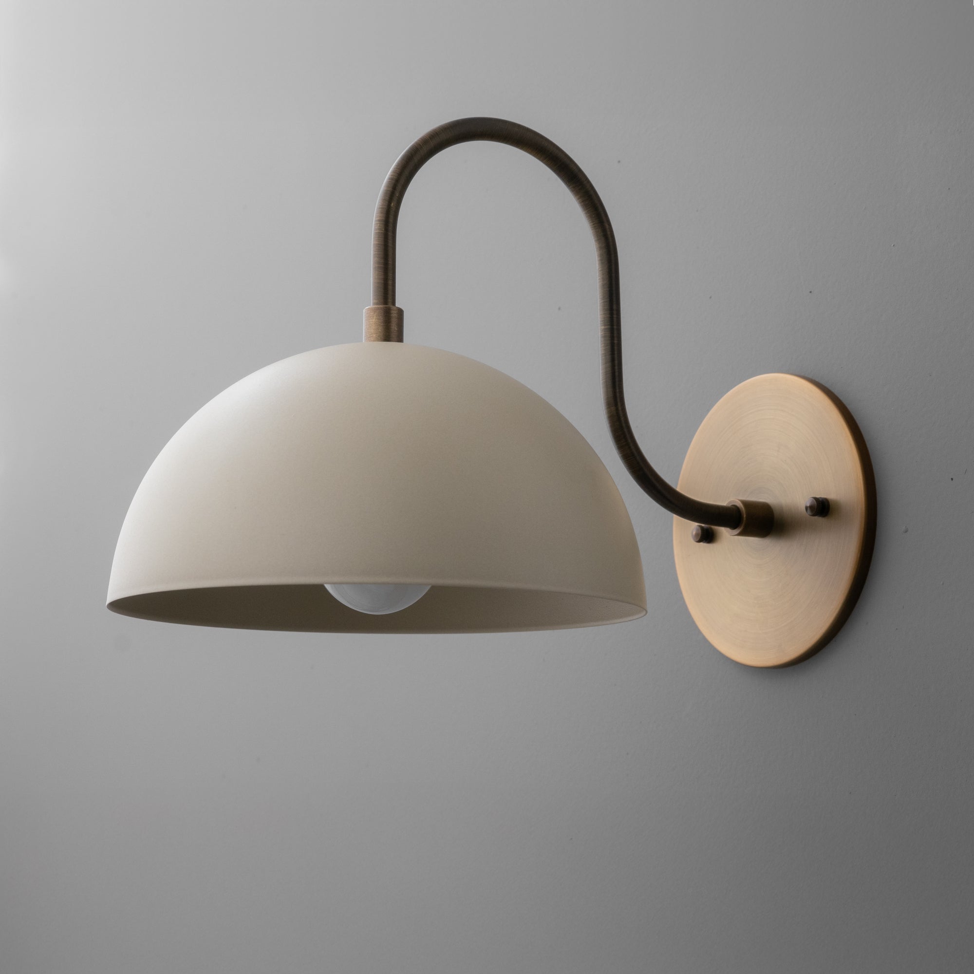Wall sconce with matte cream dome shade and curved antique brass arm mounted on round brass backplate. - SCONCE MODEL NO. 9092