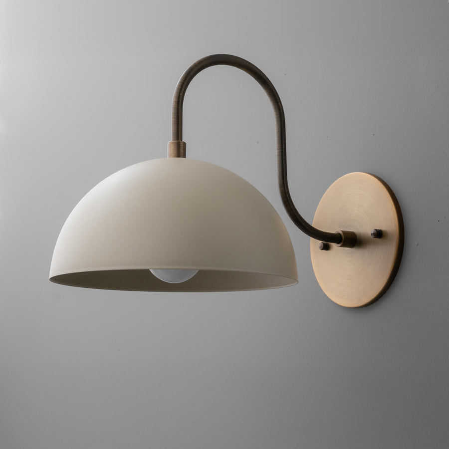 Wall sconce with matte cream dome shade and curved antique brass arm mounted on round brass backplate. - SCONCE MODEL NO. 9092