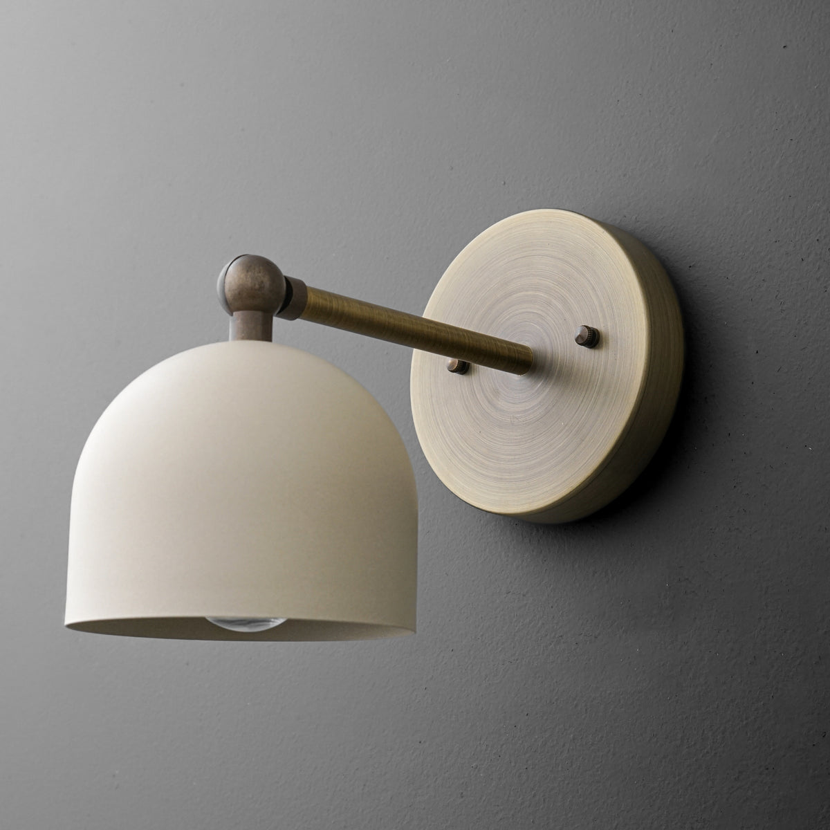 Brushed brass wall sconce with a matte cream dome shade and round mounting plate against dark gray wall. - SCONCE MODEL NO. 5103