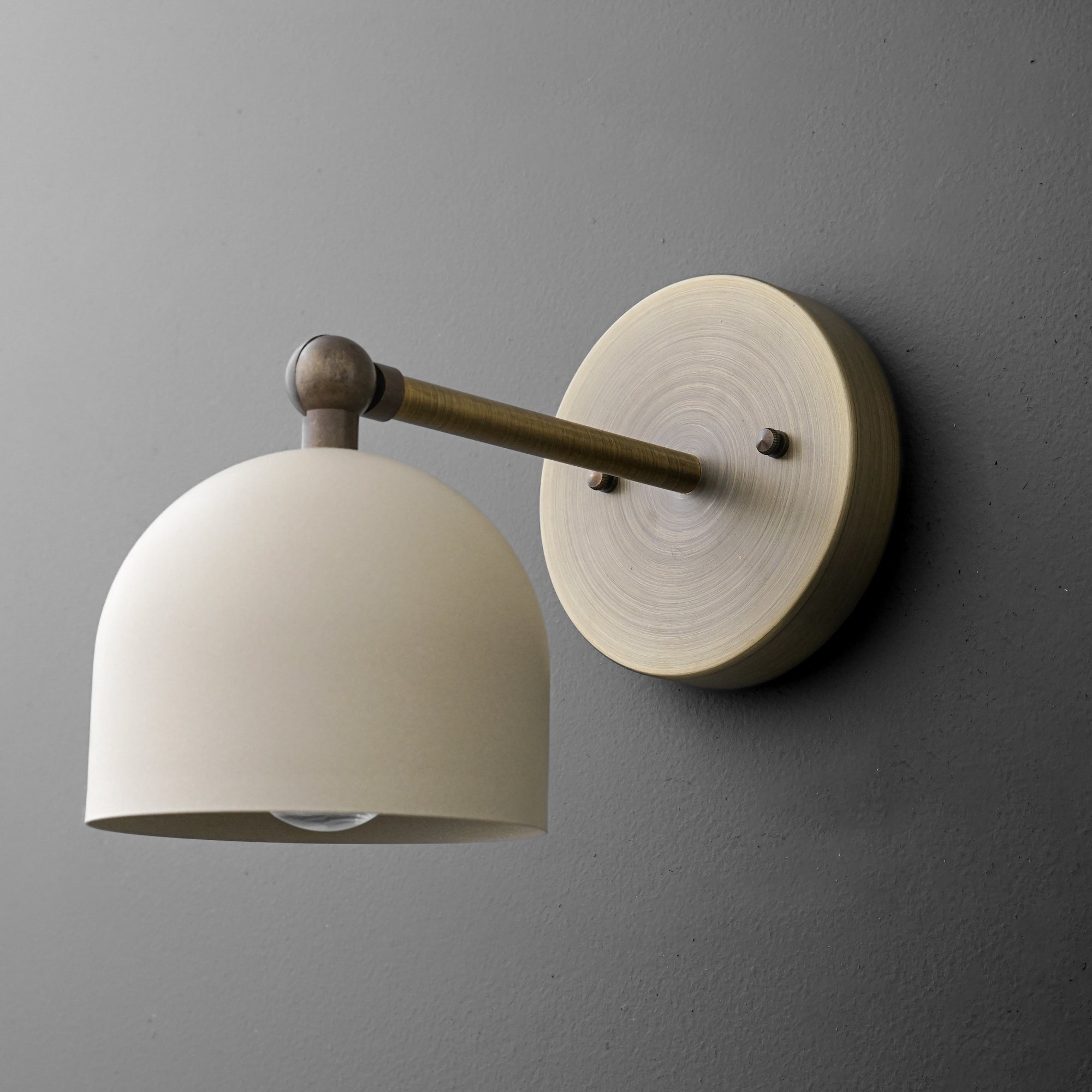 Brushed brass wall sconce with a matte cream dome shade and round mounting plate against dark gray wall. - SCONCE MODEL NO. 5103