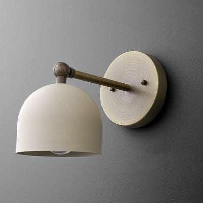 Brushed brass wall sconce with a matte cream dome shade and round mounting plate against dark gray wall. - SCONCE MODEL NO. 5103