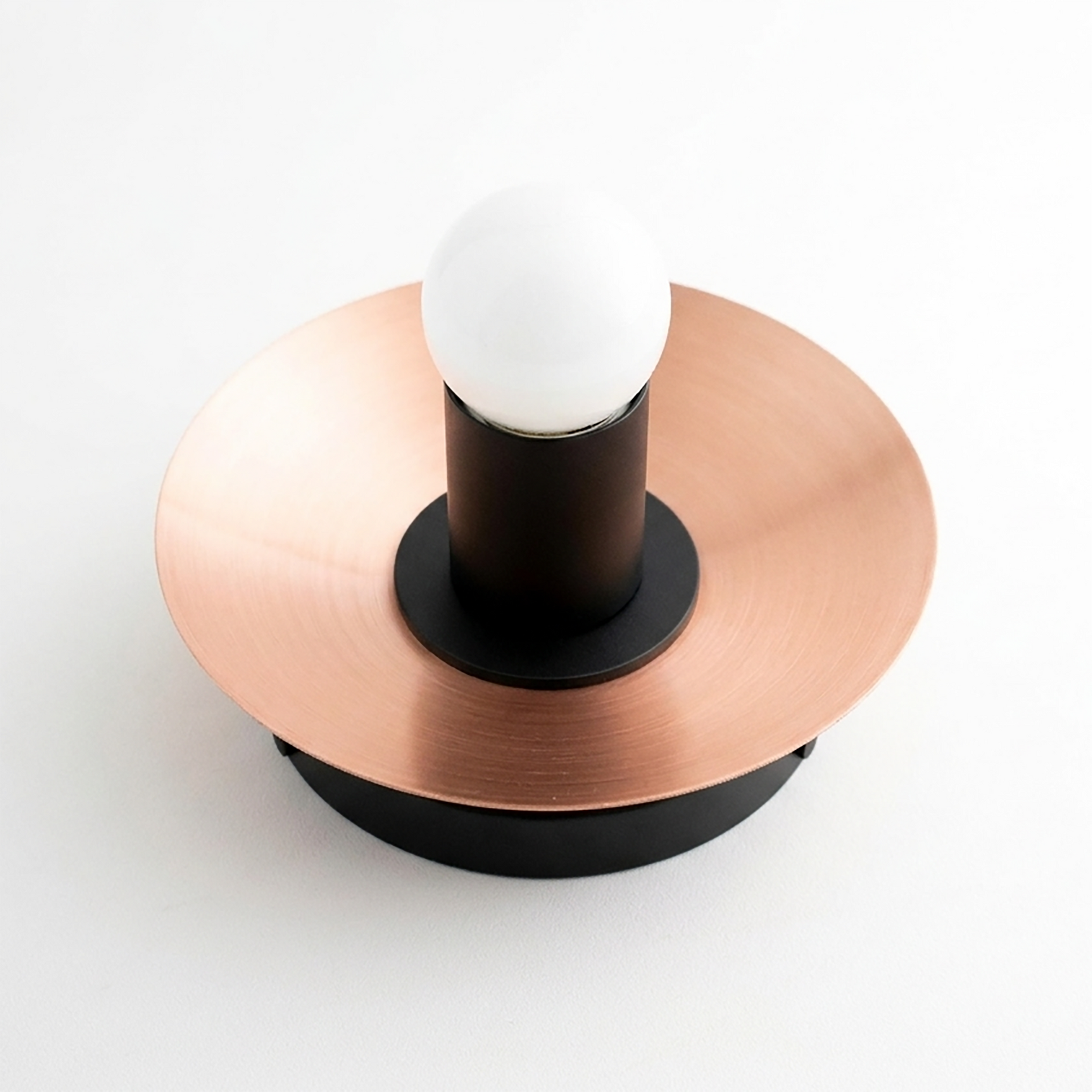 Round copper flush mount wall sconce with black cylindrical base and exposed white bulb. - SCONCE MODEL NO. 7004