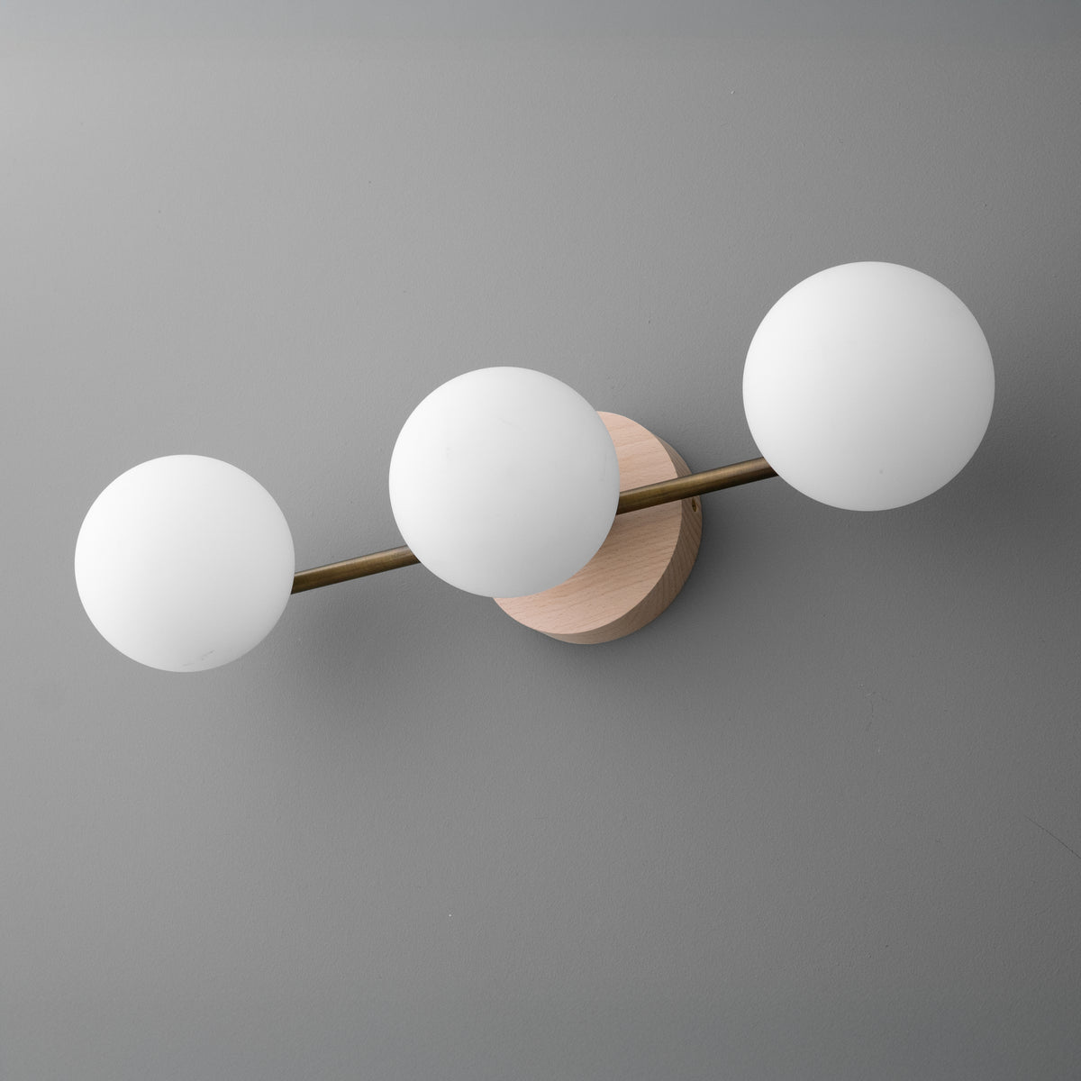 Three-bulb vanity light with frosted white glass globes on a brushed brass horizontal bar and round beige wall mount. - VANITY LIGHT MODEL NO. 6089