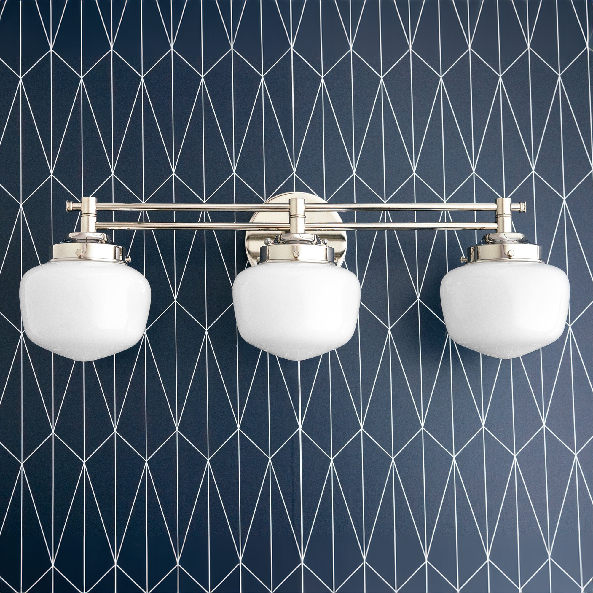Polished nickel triple vanity light with three white glass globe shades in Art Deco style against a navy geometric wall. - VANITY LIGHT MODEL NO. 4352