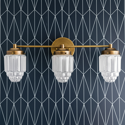 Three-bulb vanity light with raw brass finish and tiered glass globe shades against geometric wallpaper background. - VANITY LIGHT MODEL NO. 3918