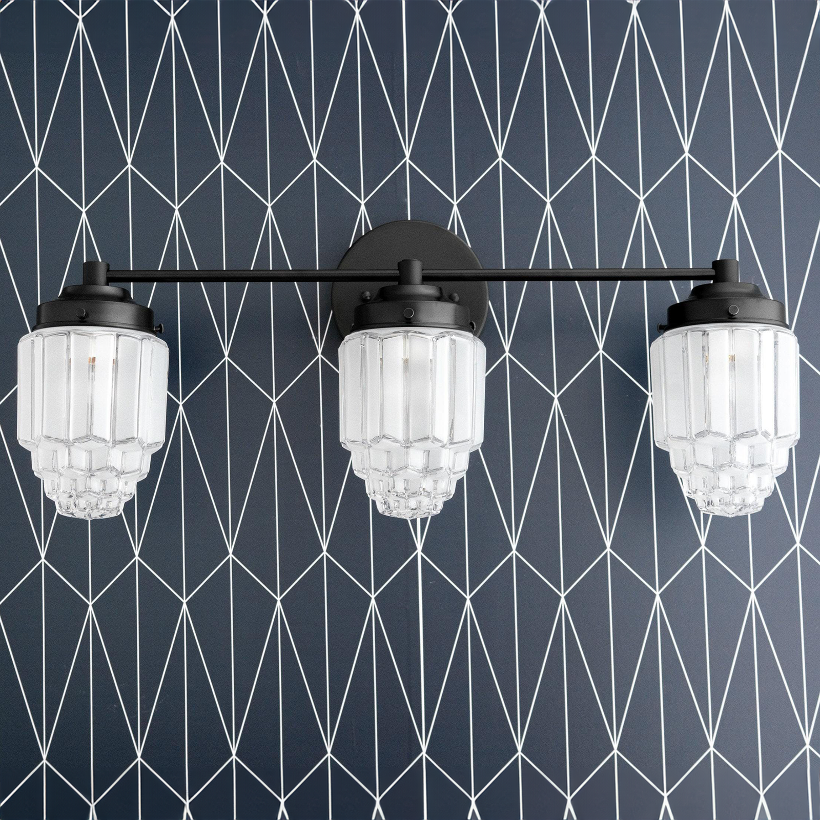 Black metal vanity light with three tiered globe glass shades against geometric wallpaper. - VANITY LIGHT MODEL NO. 3918