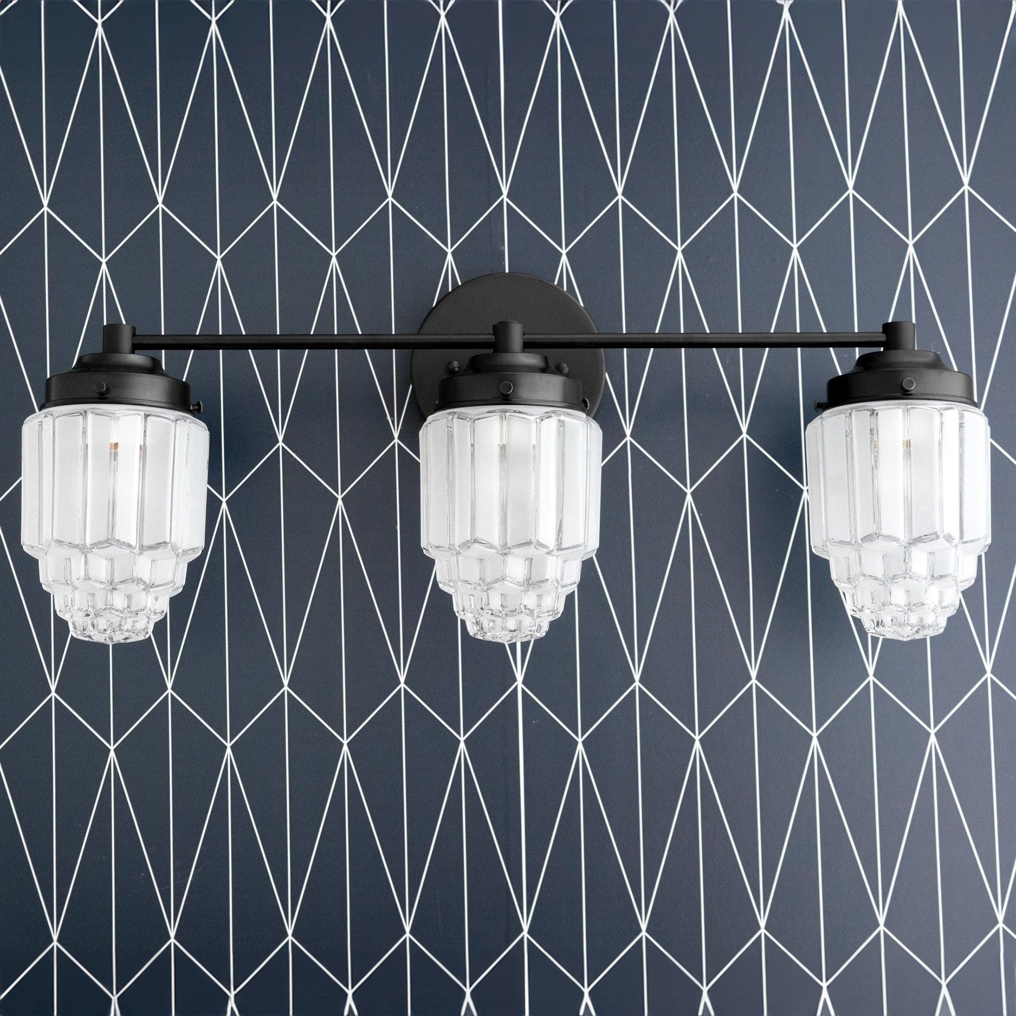 Black metal vanity light with three tiered globe glass shades against geometric wallpaper. - VANITY LIGHT MODEL NO. 3918