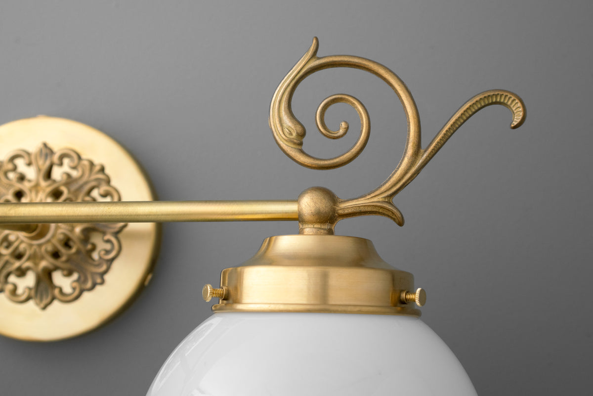 Brushed gold metal vanity light with decorative scroll arm and white frosted glass globe shade. - VANITY LIGHT MODEL NO. 1135