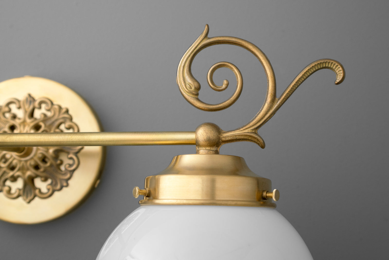 Brushed gold metal vanity light with decorative scroll arm and white frosted glass globe shade. - VANITY LIGHT MODEL NO. 1135