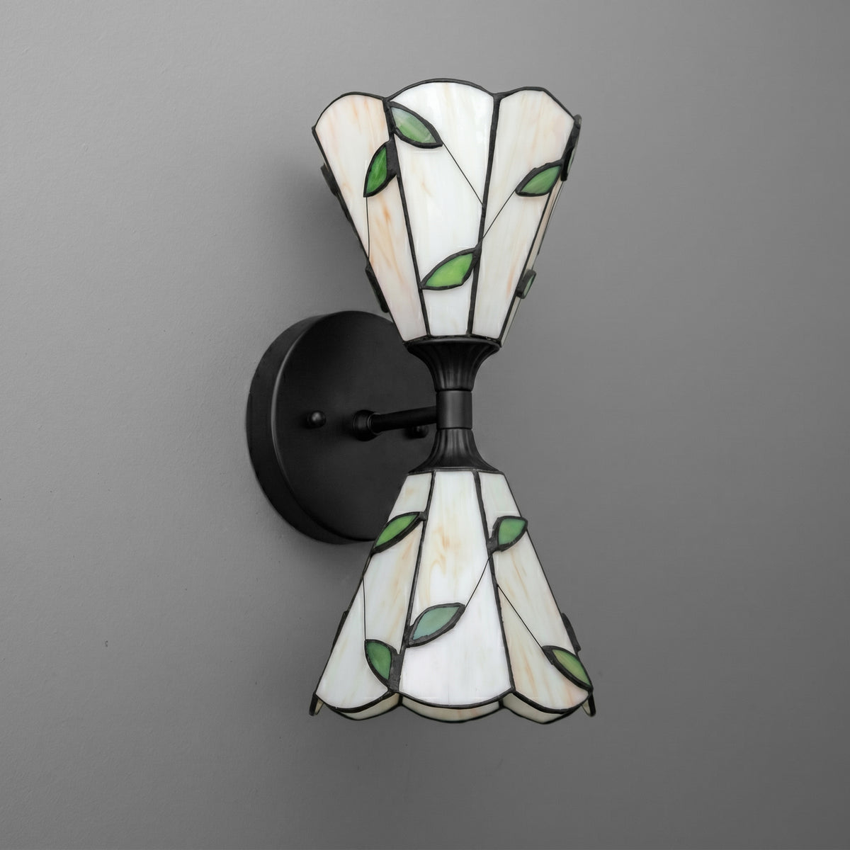 Black metal wall sconce with two stained glass shades featuring white panels and green leaf patterns. - SCONCE MODEL NO. 8621