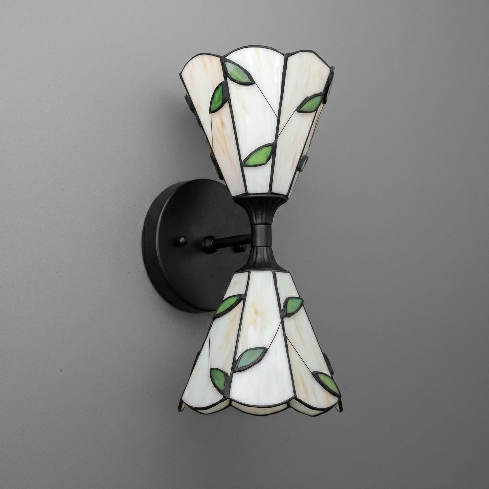 Black metal wall sconce with two stained glass shades featuring white panels and green leaf patterns. - SCONCE MODEL NO. 8621