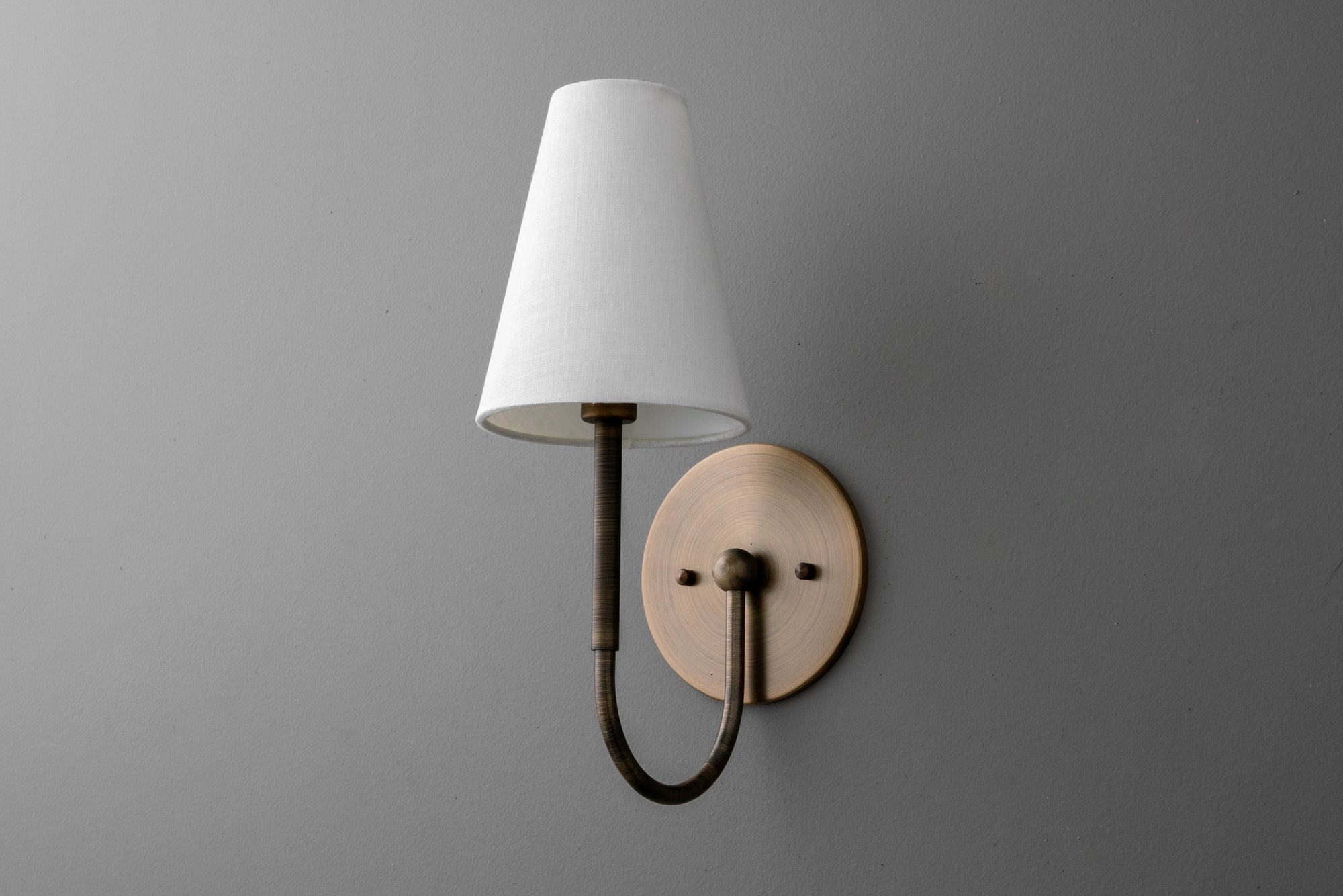 Wall sconce with curved antique brass arm and white tapered fabric shade mounted on round brass backplate. - SCONCE MODEL NO. 4594