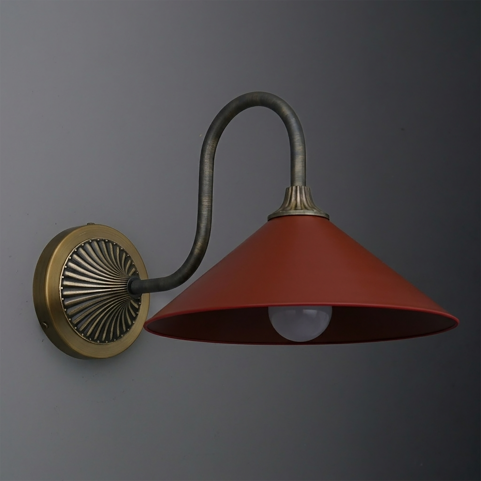 Wall-mounted sconce with a curved bronze arm, round brass base, and wide red metal shade. - SCONCE MODEL NO. 1031