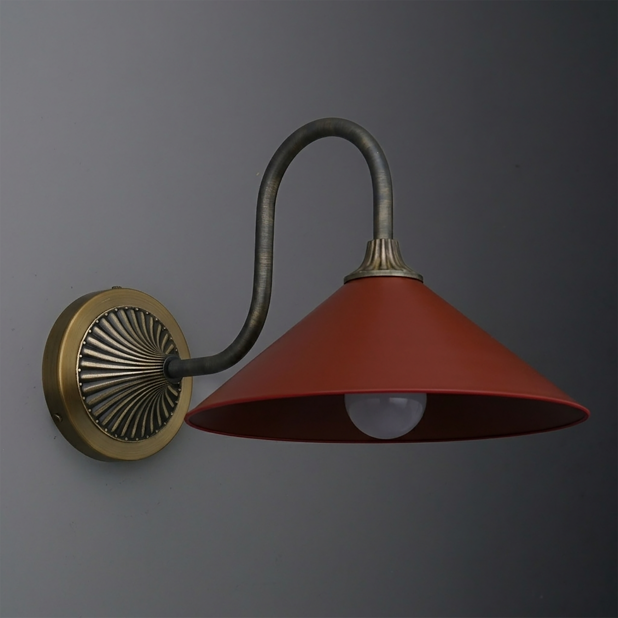Wall-mounted sconce with a curved bronze arm, round brass base, and wide red metal shade. - SCONCE MODEL NO. 1031