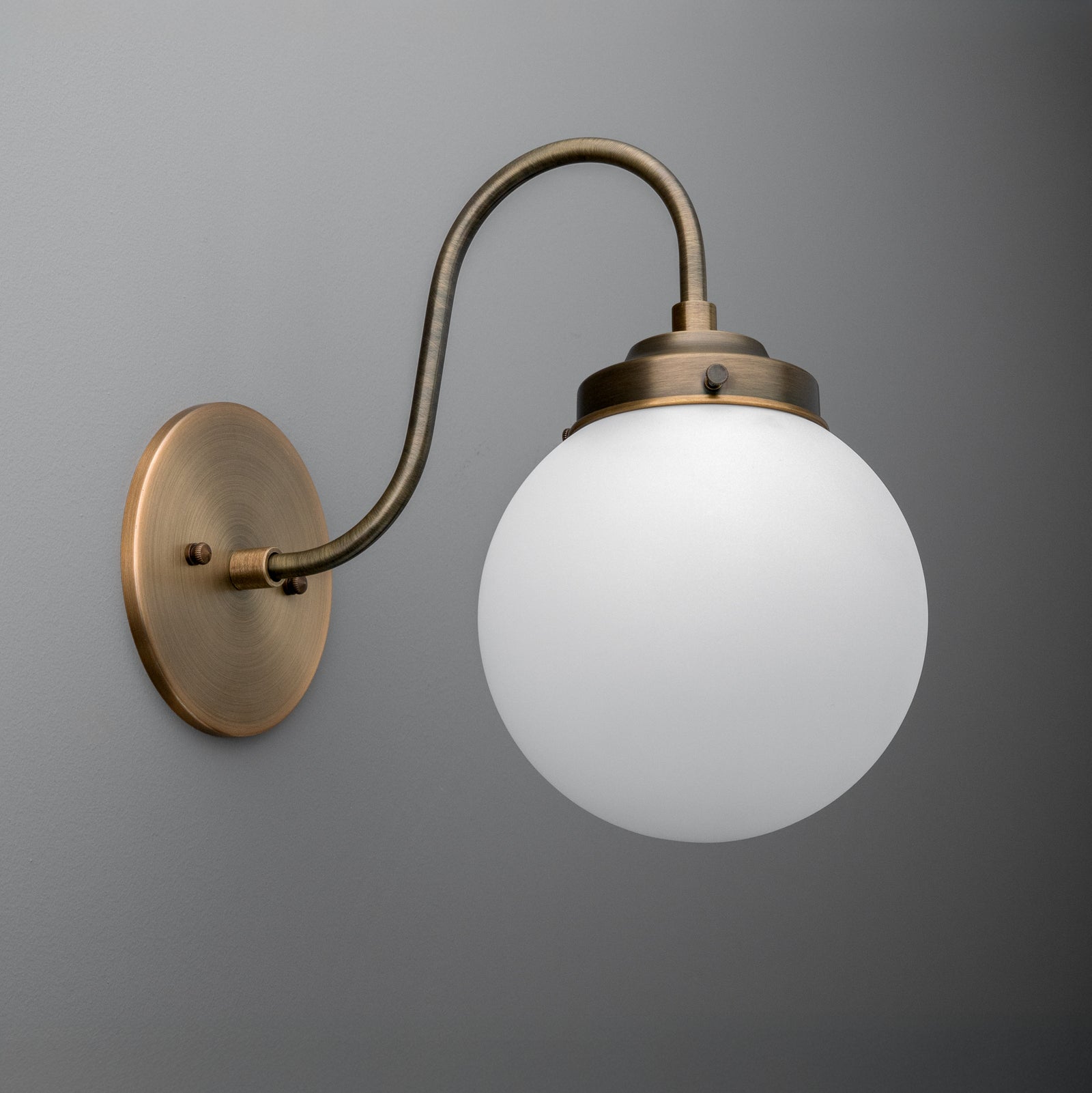 Antique brass wall sconce with a curved arm and frosted white glass globe shade. - SCONCE MODEL NO. 1886