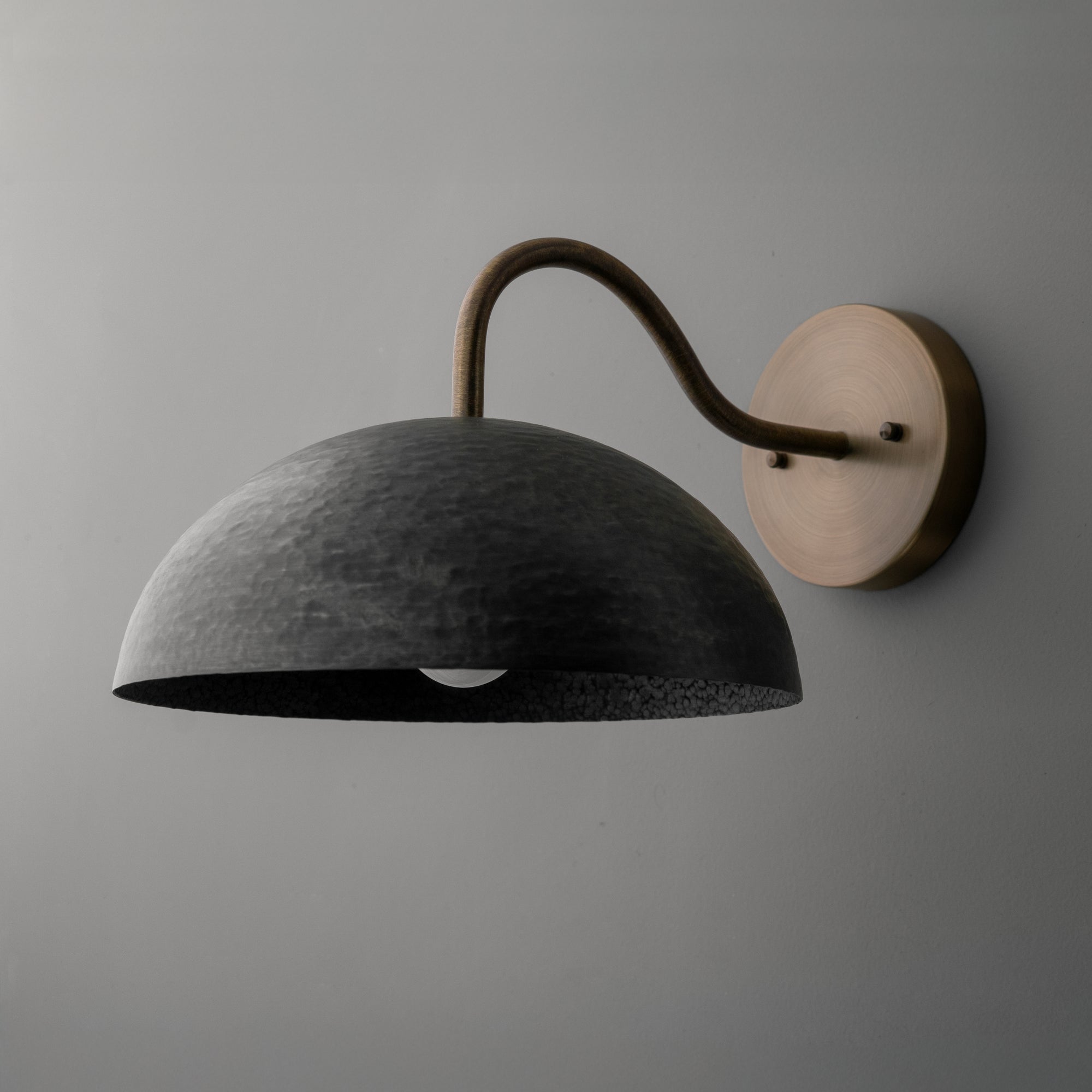 Wall sconce with a dark textured dome shade and curved metal arm mounted on a round base. - SCONCE MODEL NO. 9874